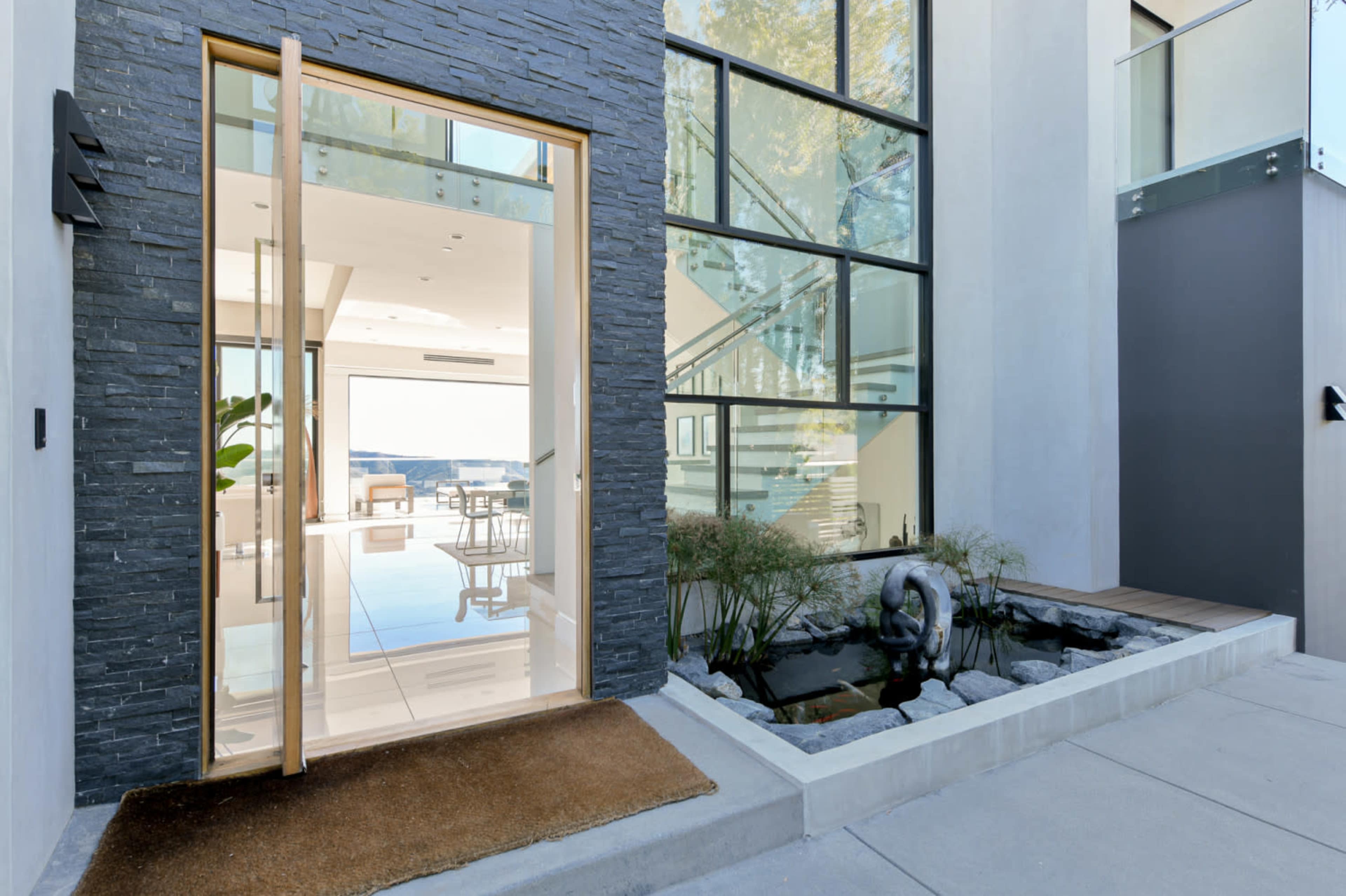 A modern entrance with a large glass door leading to a bright, minimalist interior, accompanied by a small decorative pond and greenery at the front.