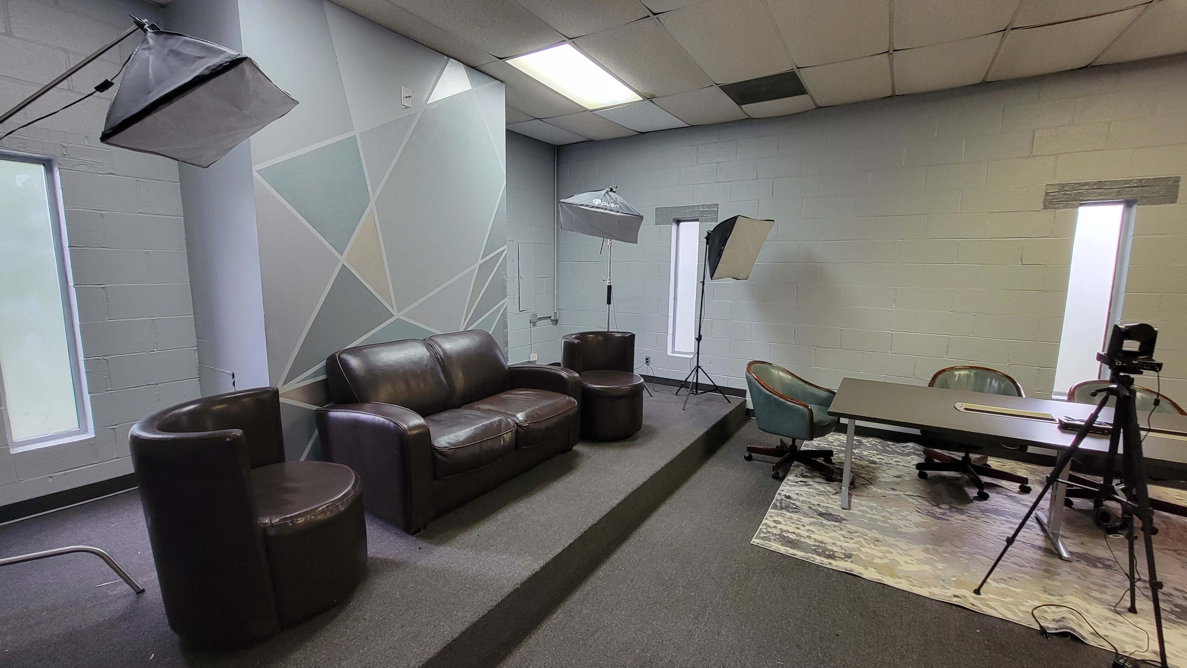 A well-lit room featuring a brown leather sofa, two black chairs, a round table, and photography lighting equipment set up around the space.