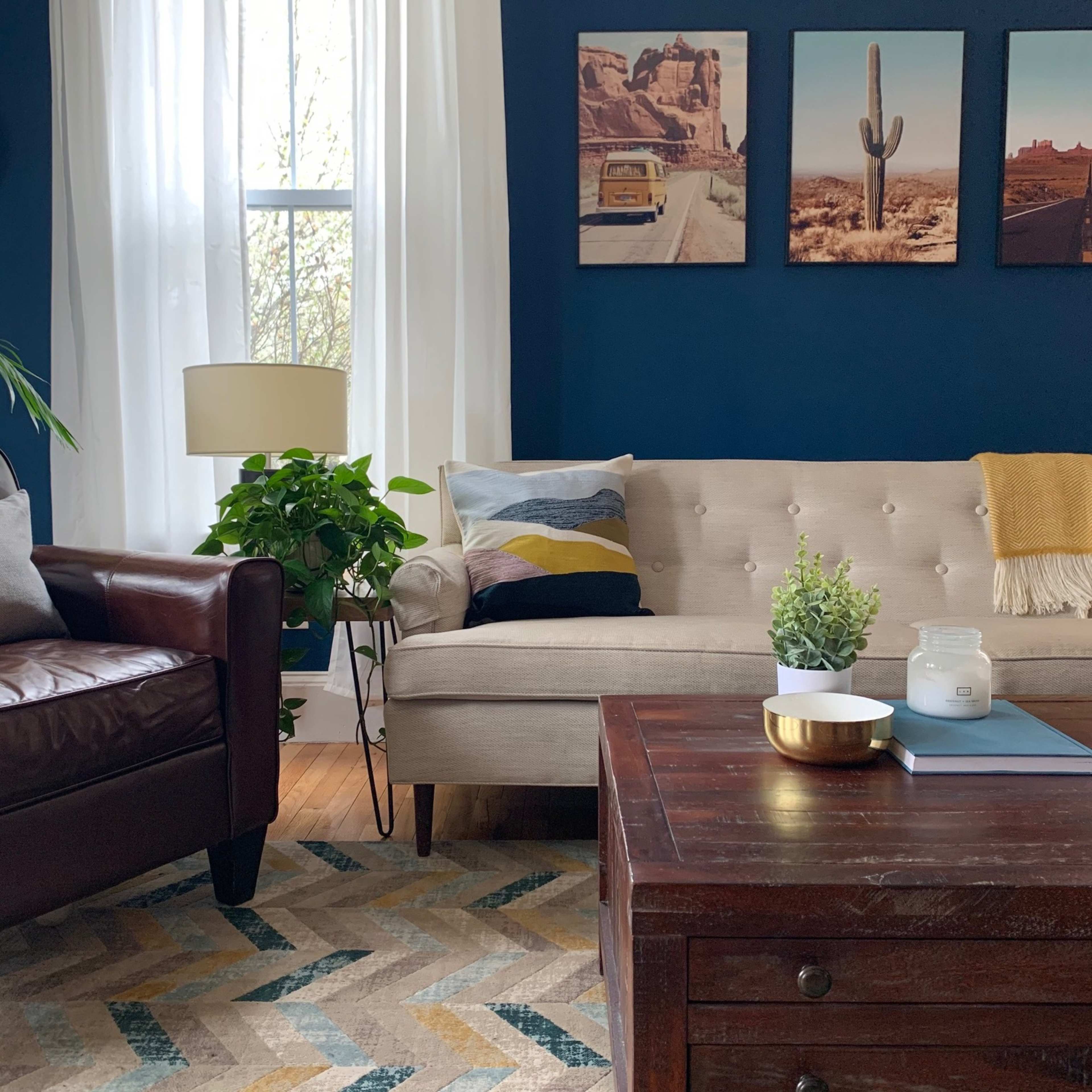 The room features a light-colored sofa, a brown leather armchair, and a wooden coffee table, with framed landscape photographs on the blue wall.