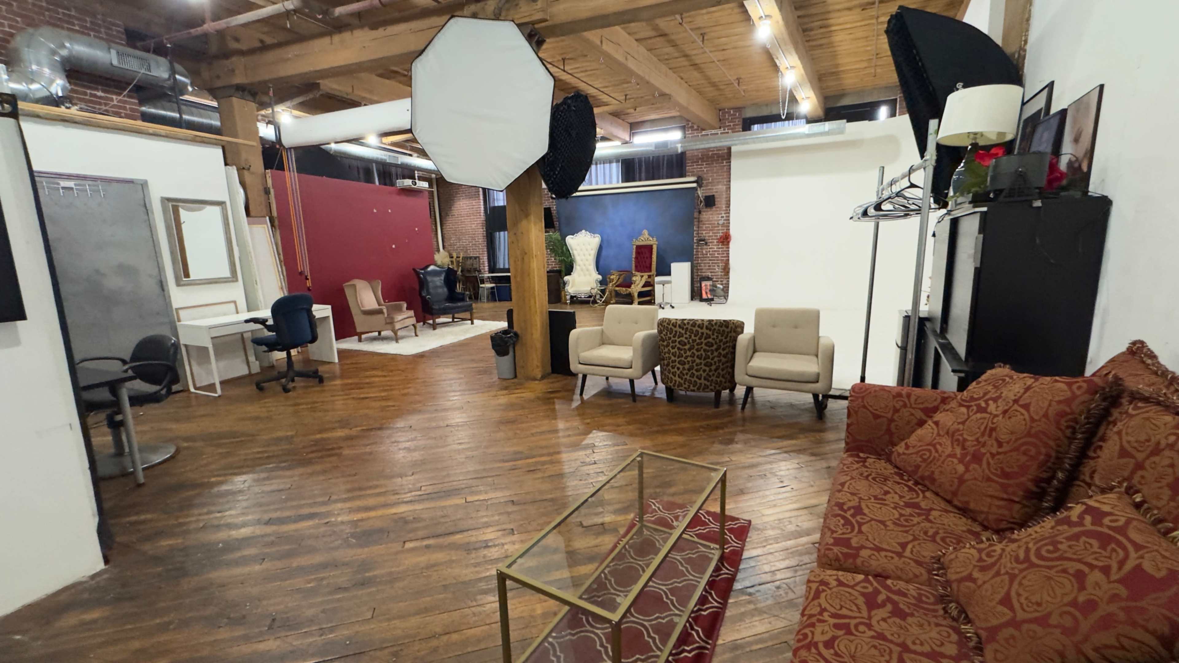 The image shows a spacious photography studio with wooden floors, comfortable seating areas, and various backdrops set up for shooting.
