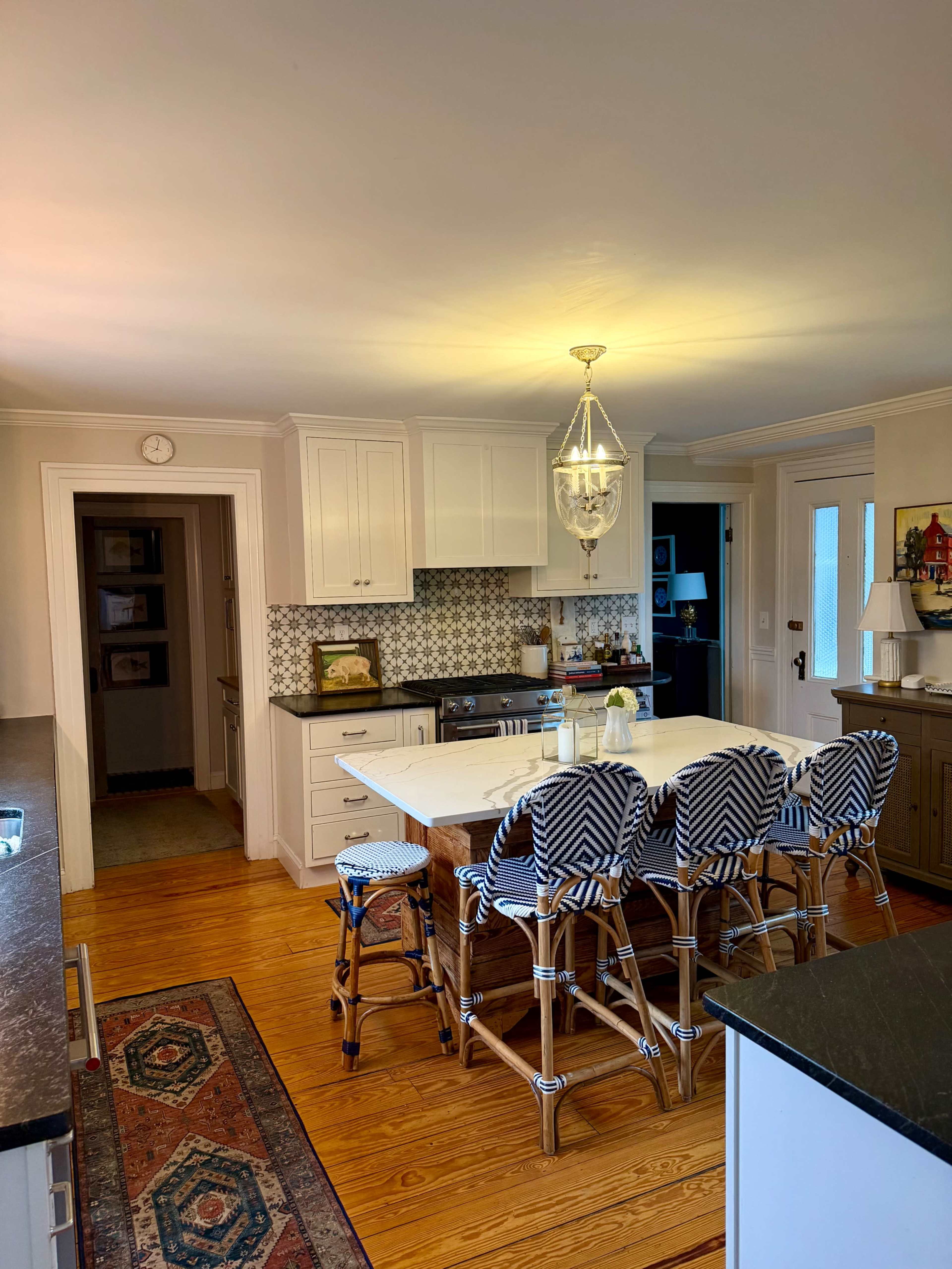 A spacious kitchen features a central island with bar stools, light cabinetry, and patterned backsplash tiles.