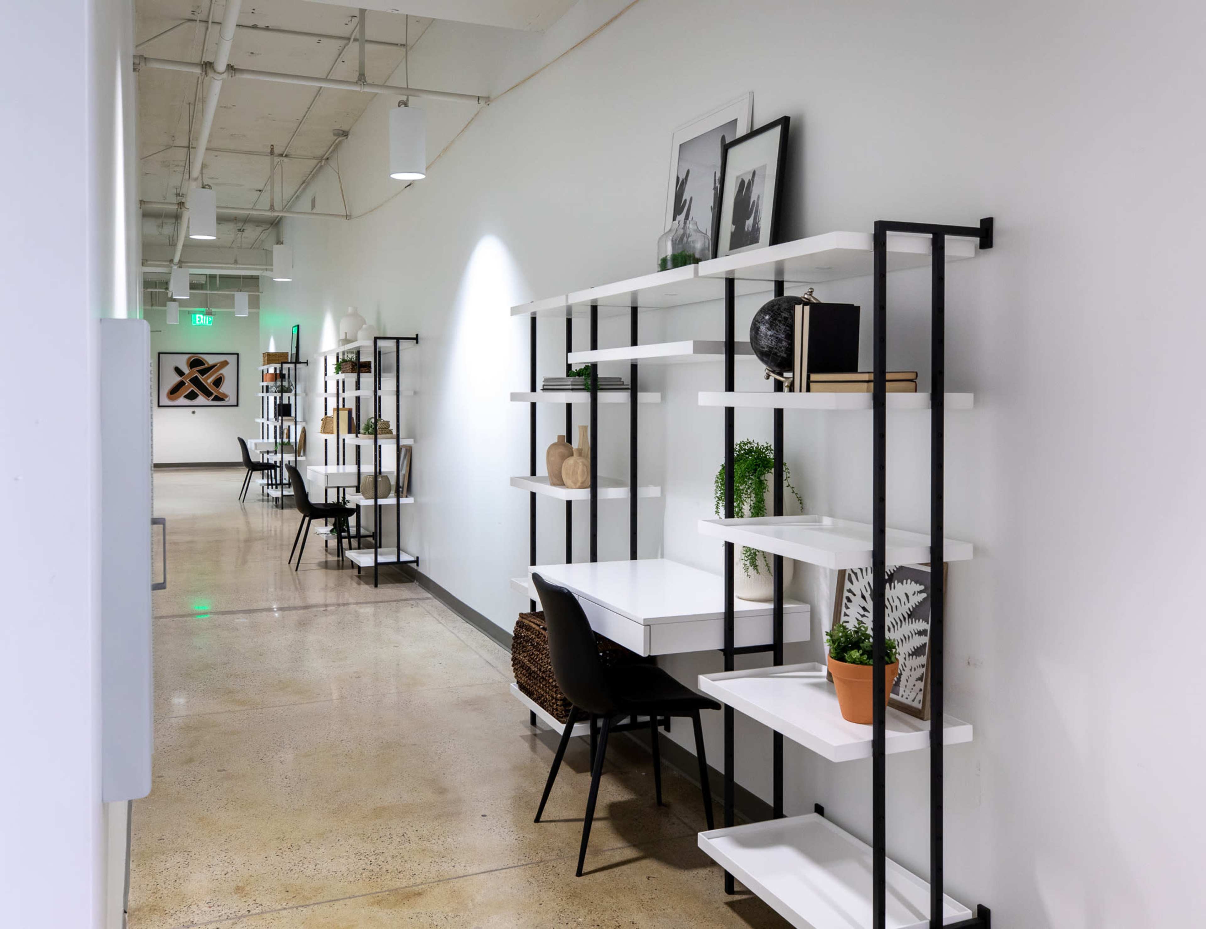 A hallway lined with white shelves and minimalist desks arranged for workspace usage.