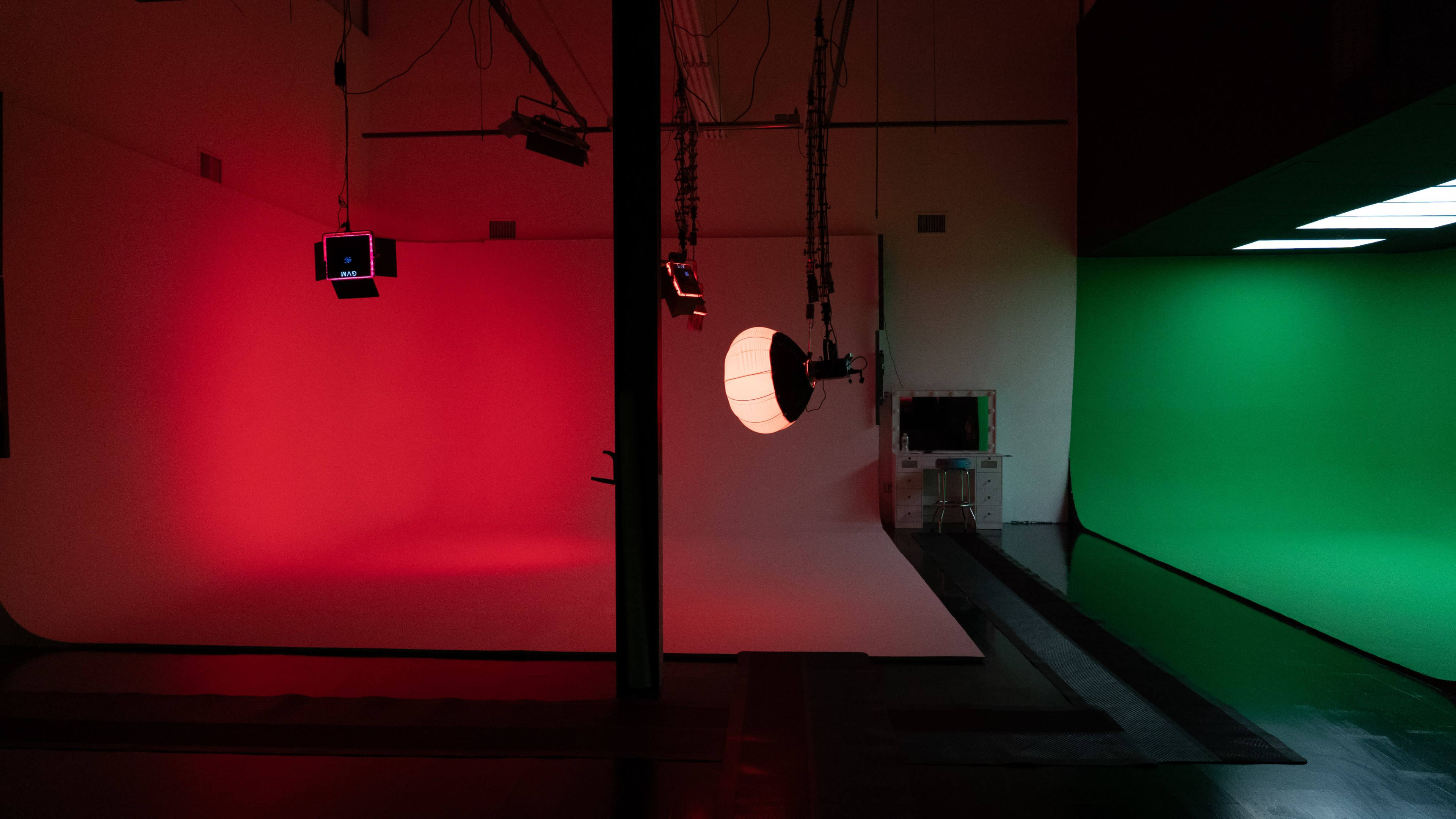 The image shows a photography studio with a red backdrop on one side and a green backdrop on the other, illuminated by various studio lights.