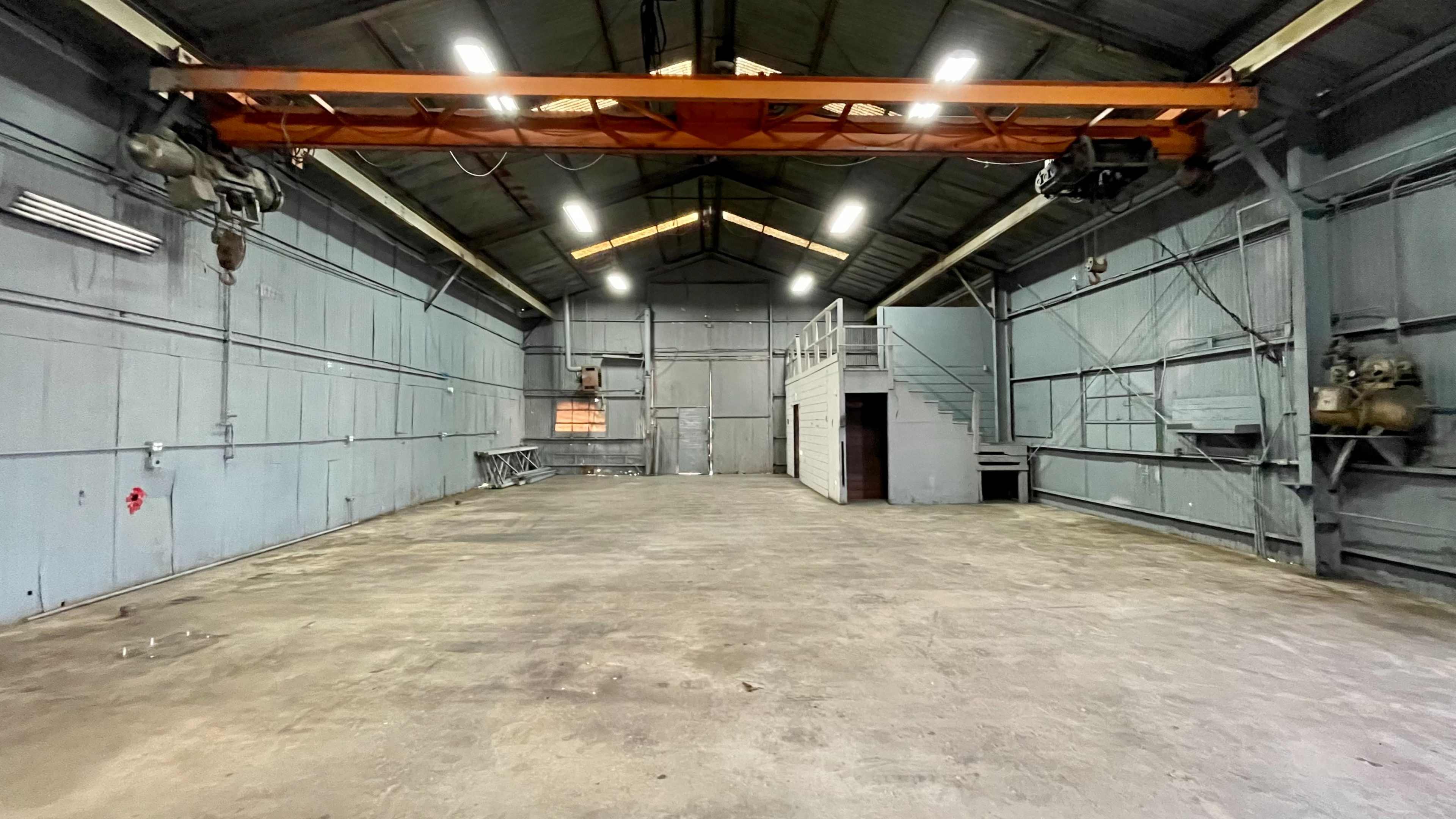 A large, empty industrial warehouse with gray walls, high ceilings, and overhead cranes.