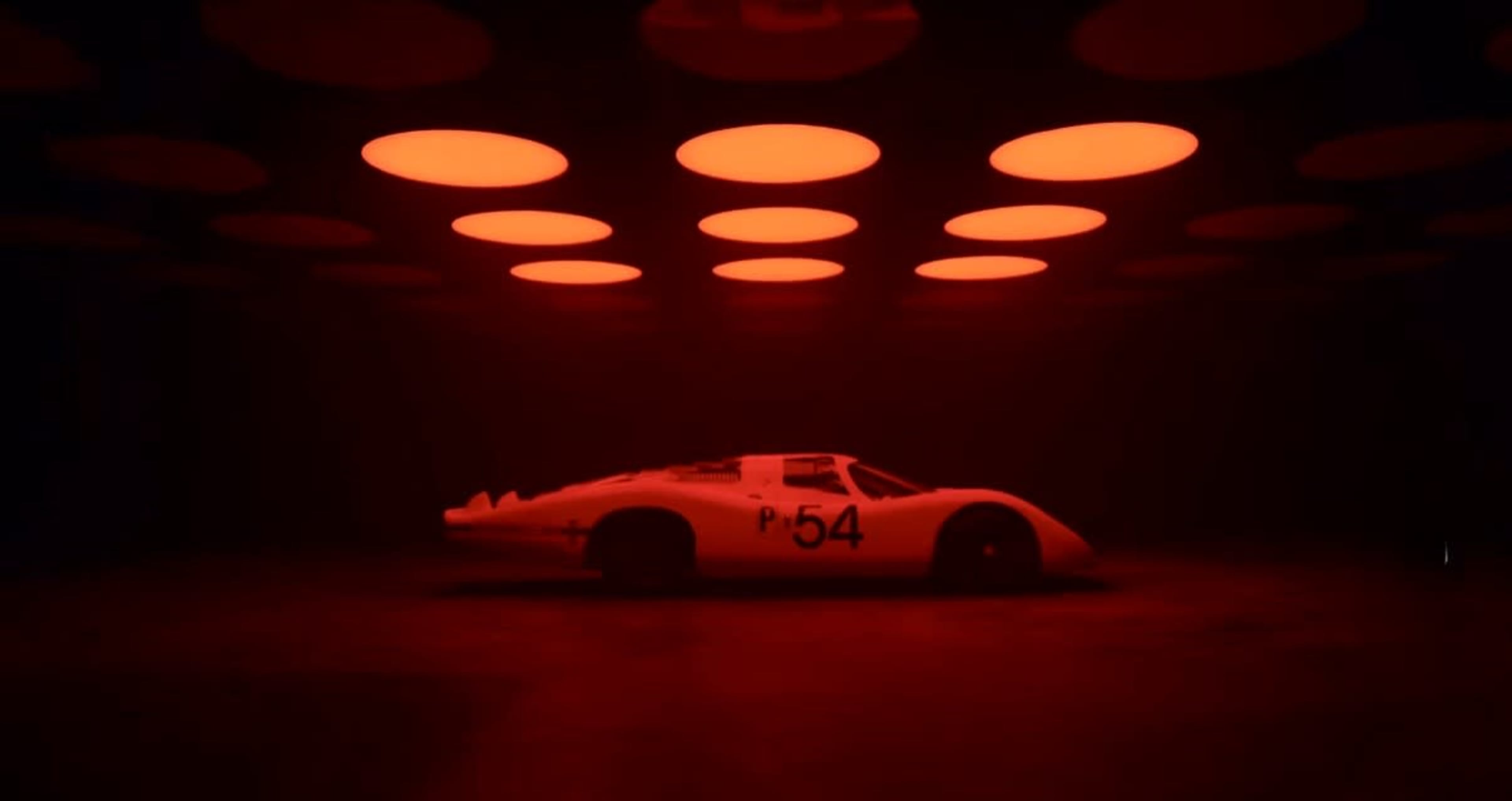 A vintage race car with the number 54 is illuminated by red circular lights in a dark environment.