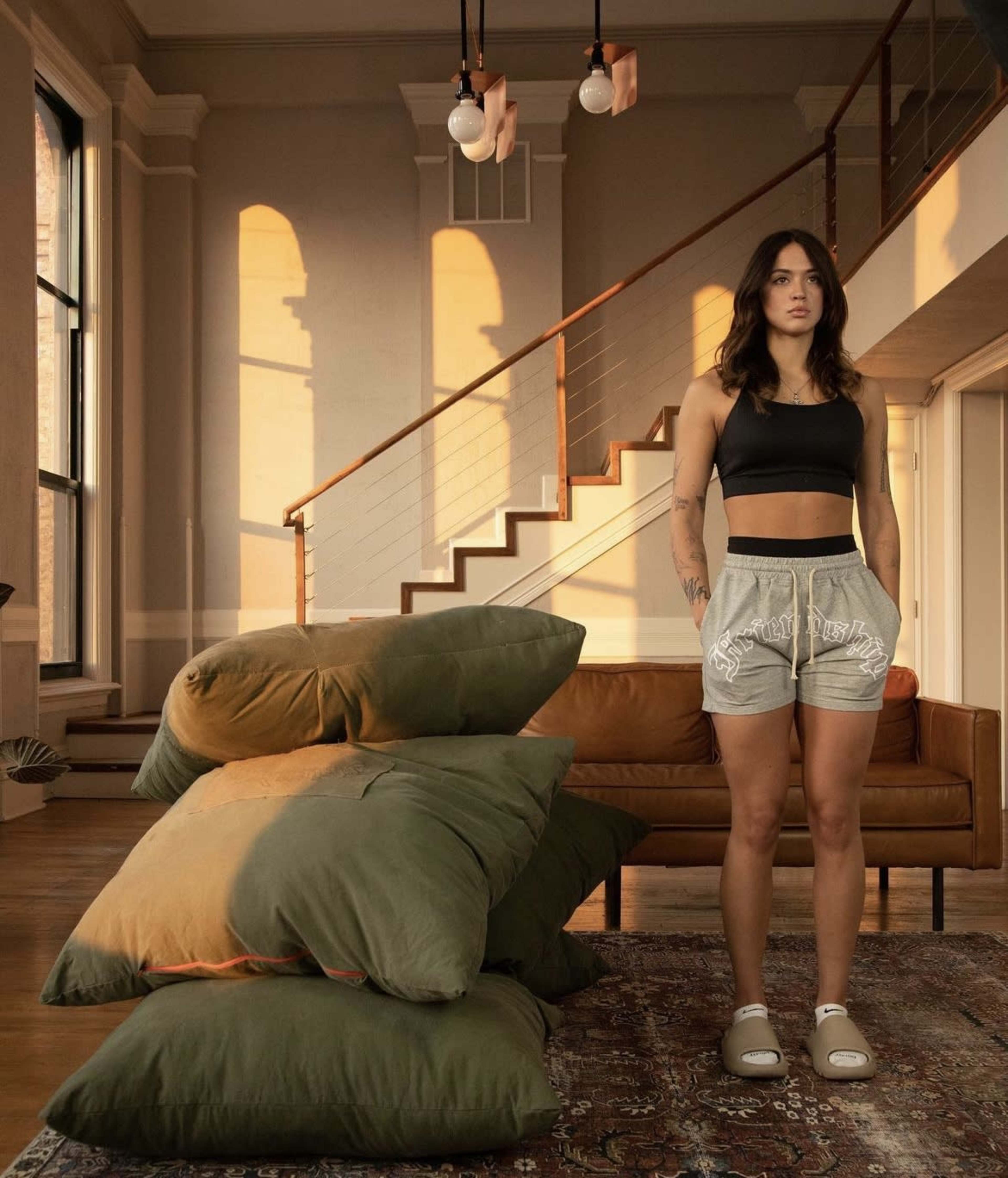 A person stands in a modern living room beside a stack of large, green cushions near a staircase.