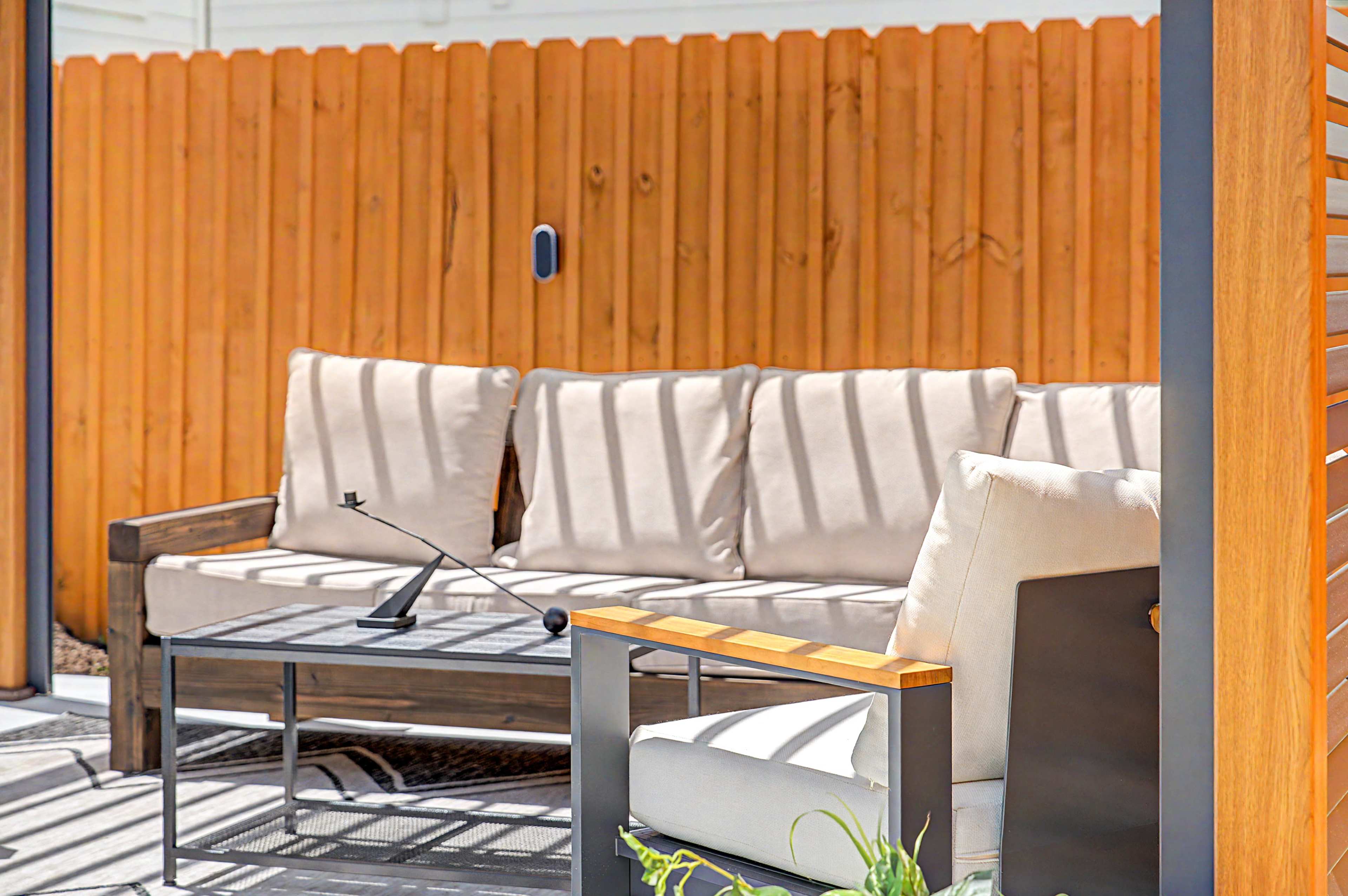 A patio area features a wooden bench with beige cushions and a matching coffee table situated in front of a wooden fence.