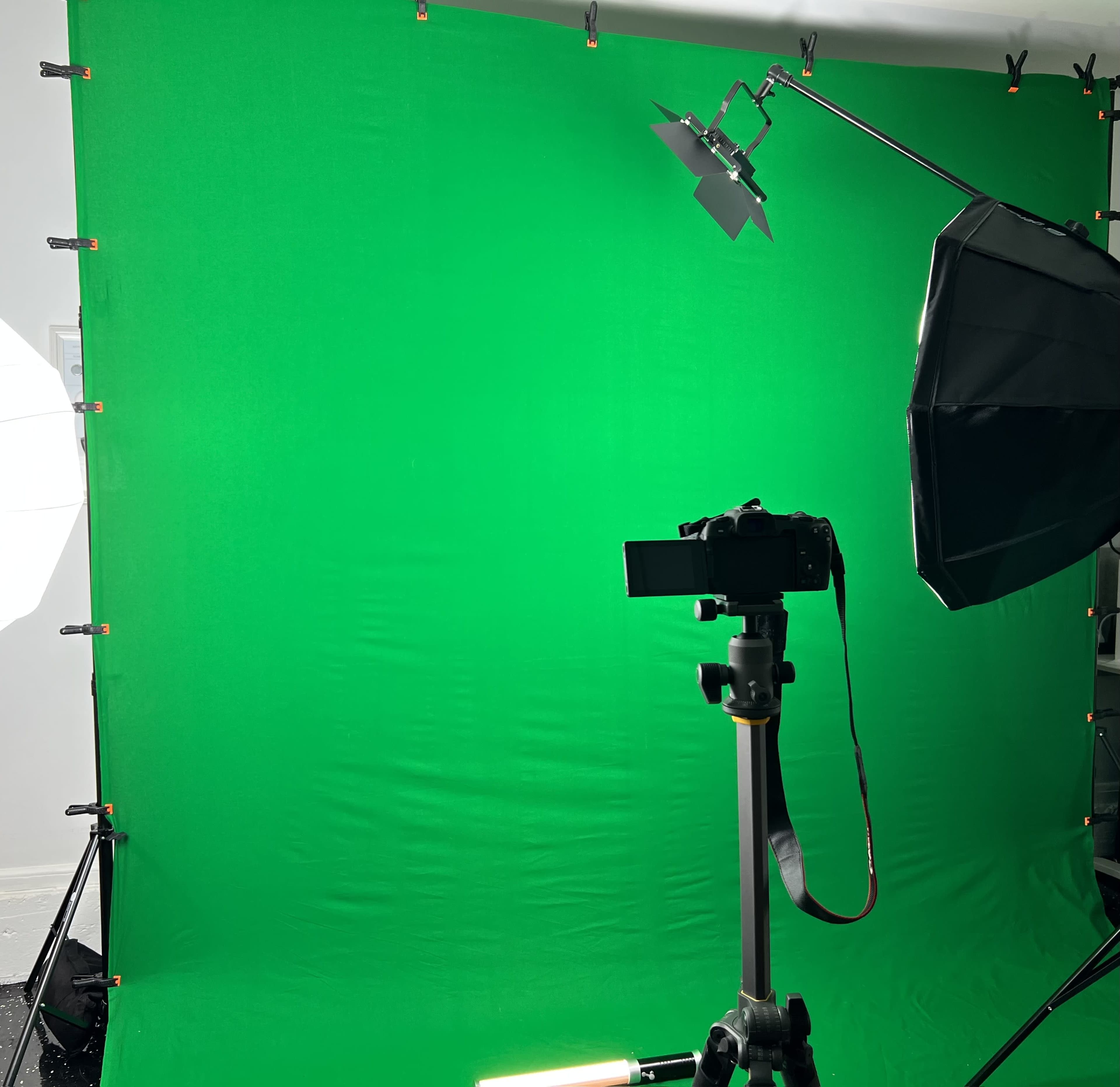 A green screen setup with a camera mounted on a tripod and lighting equipment positioned nearby.