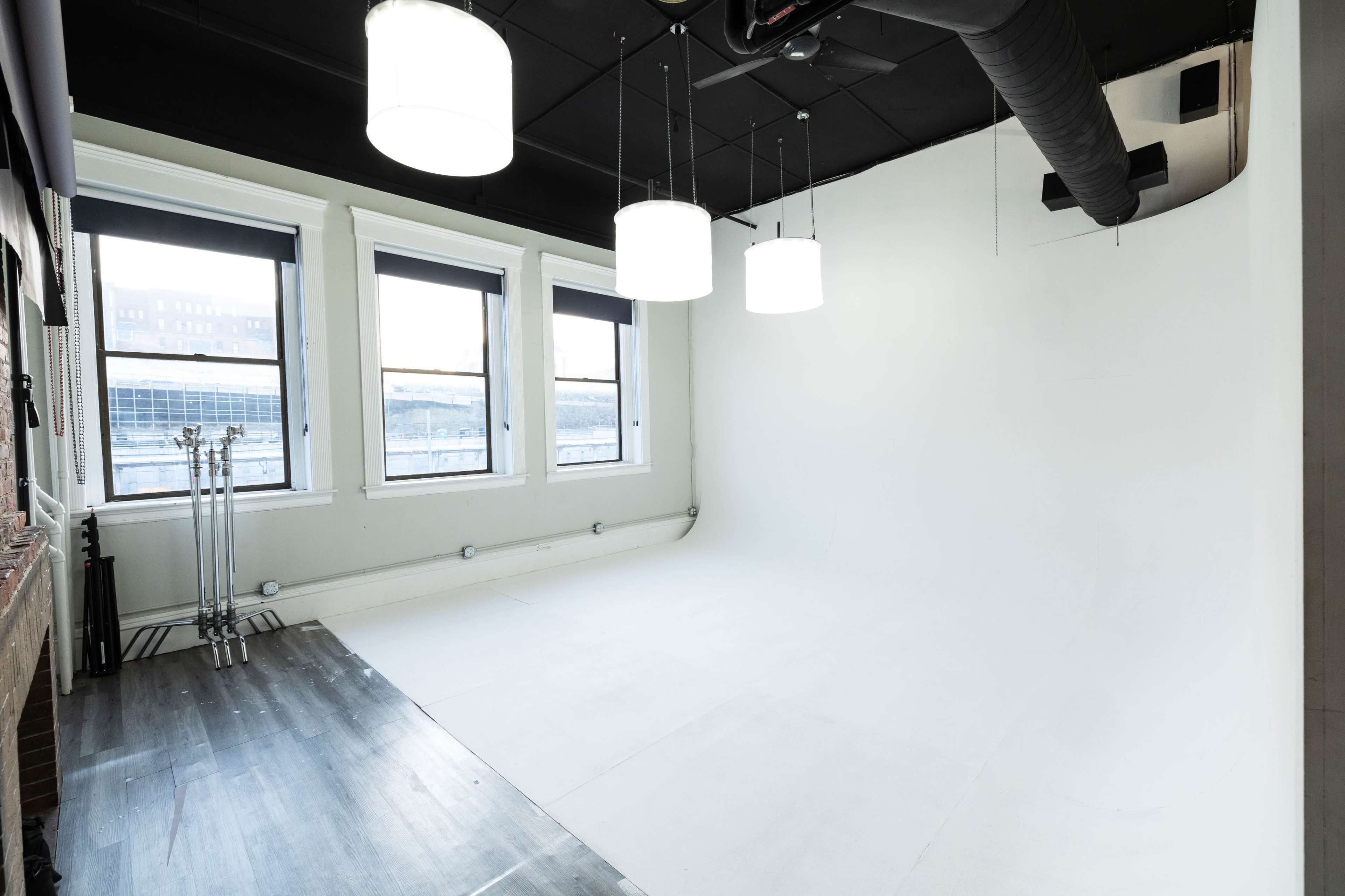 A spacious, empty studio with white walls, large windows, and overhead lights.