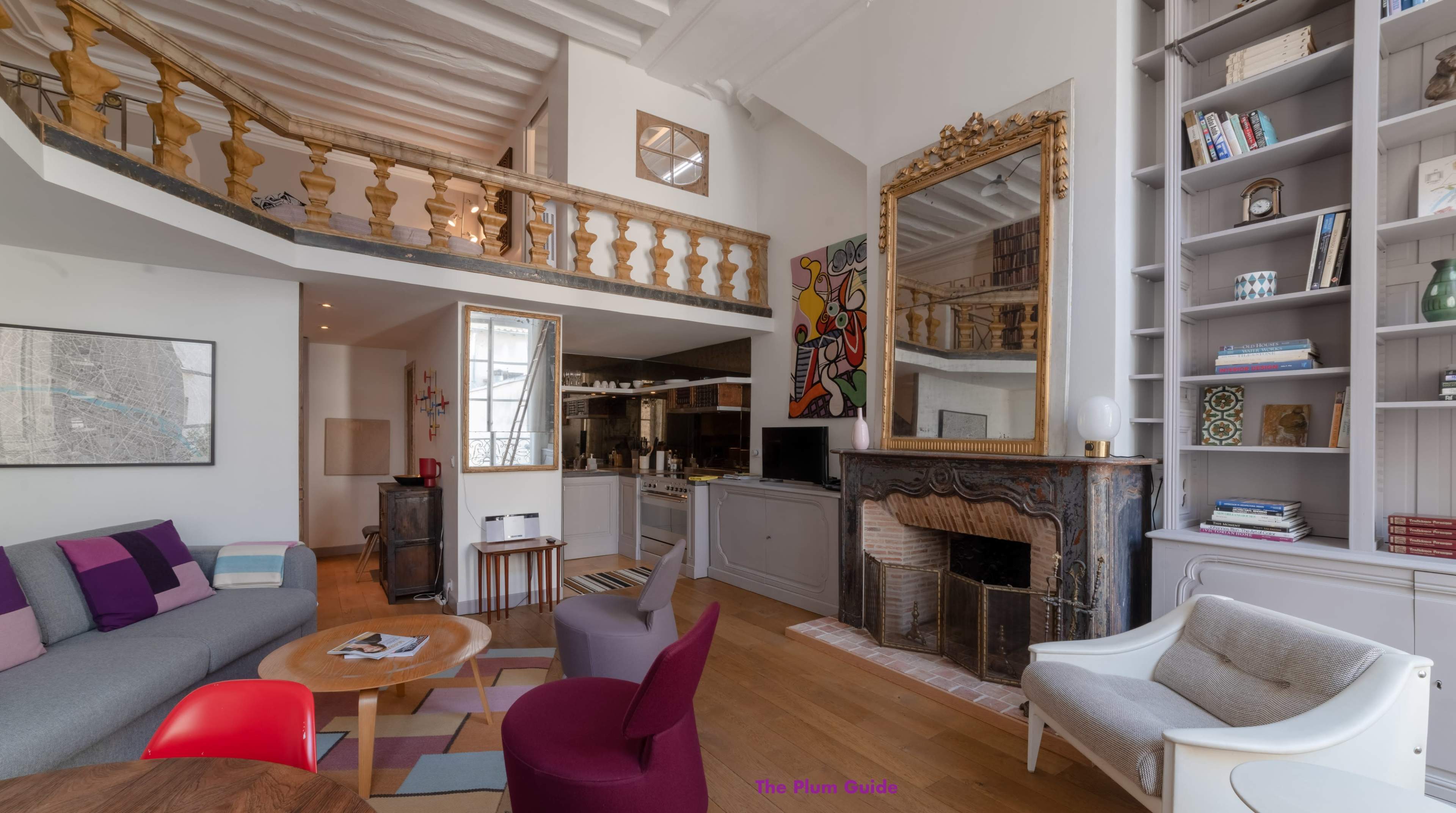 A modern living room with a fireplace, an open kitchen, and a balcony area, featuring a mix of colorful furniture and decorative elements.