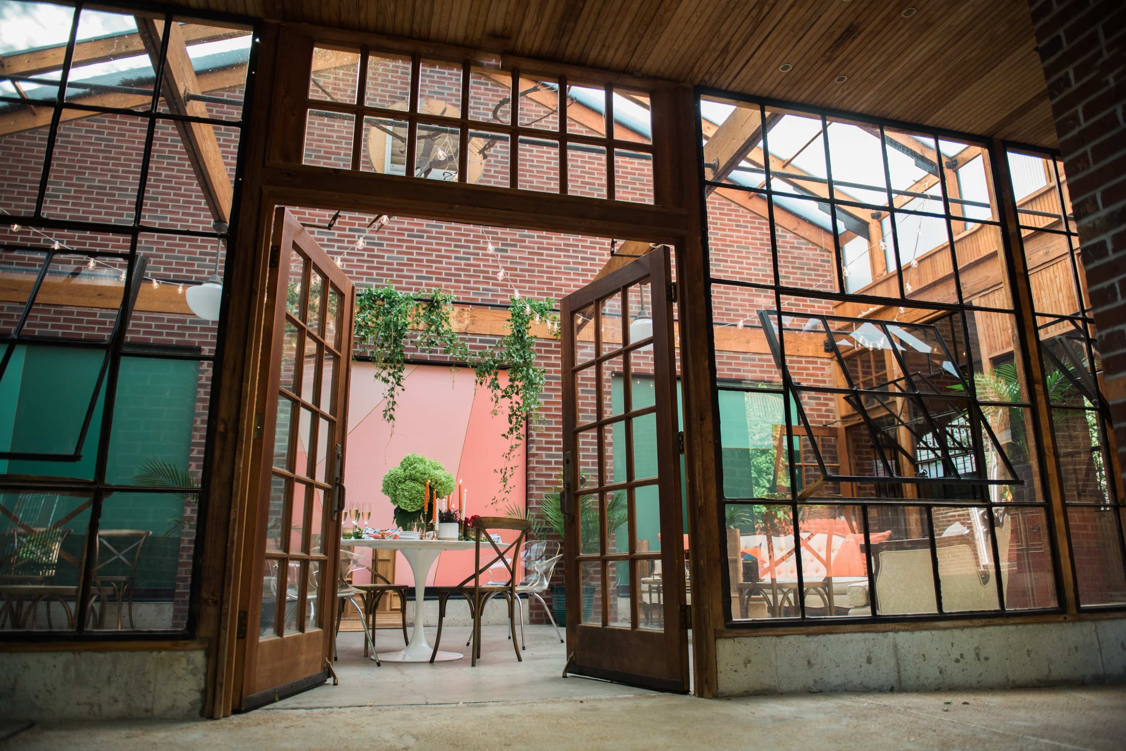 A spacious interior with large glass doors opens to a bright and colorful dining area featuring wooden furniture and greenery.