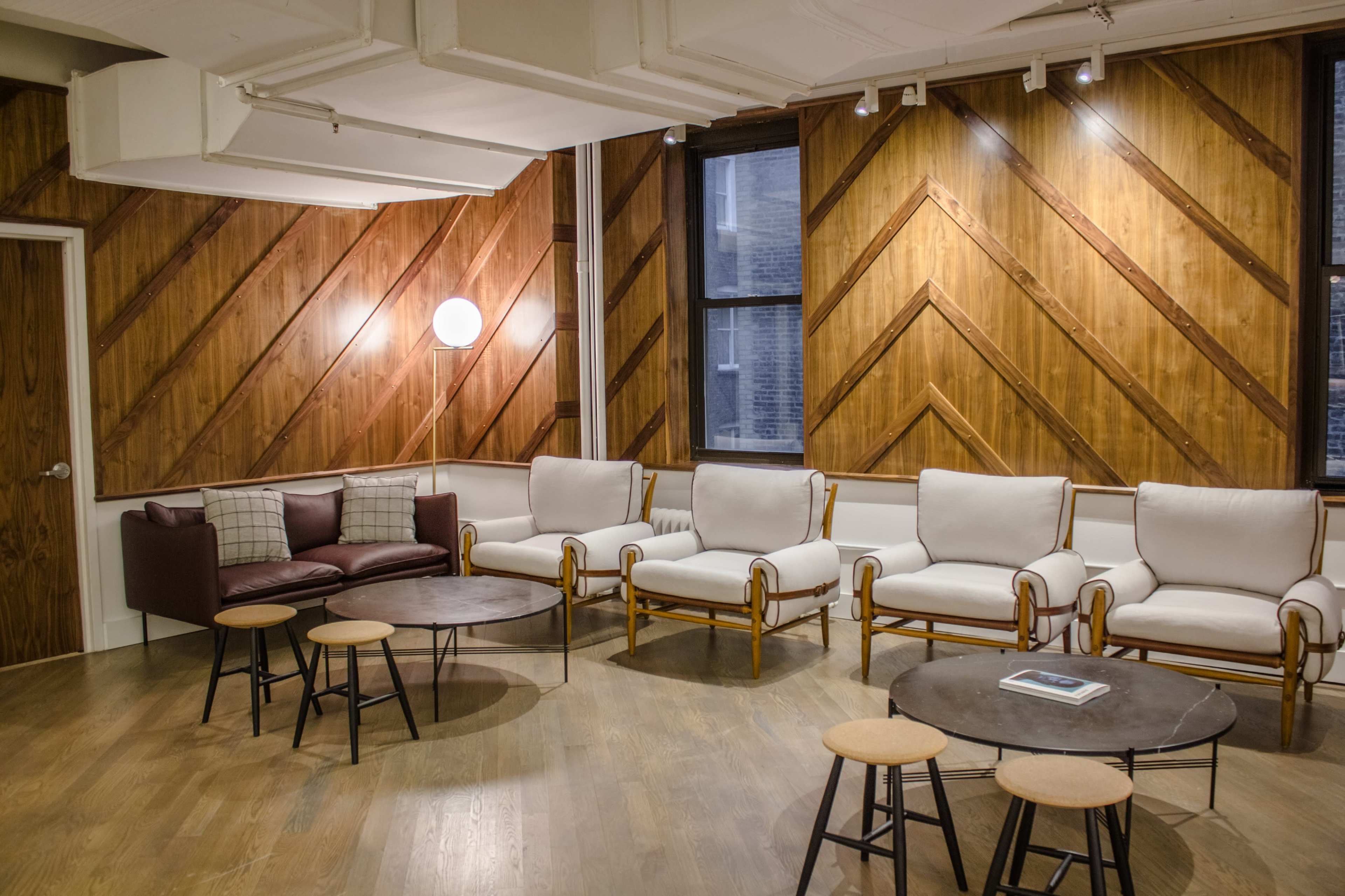The image shows a cozy lounge area with a set of neatly arranged chairs and tables against a backdrop of wood-paneled walls.