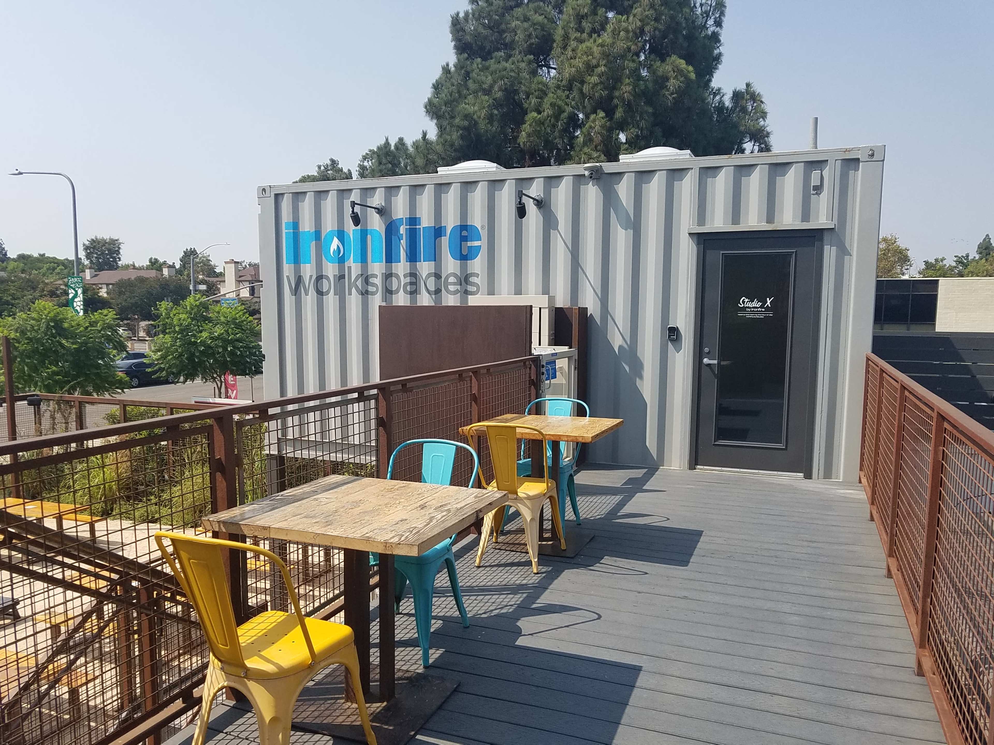 A rooftop area features two blue and yellow chairs with wooden tables beside a shipping container labeled "Ironfire Workspaces."