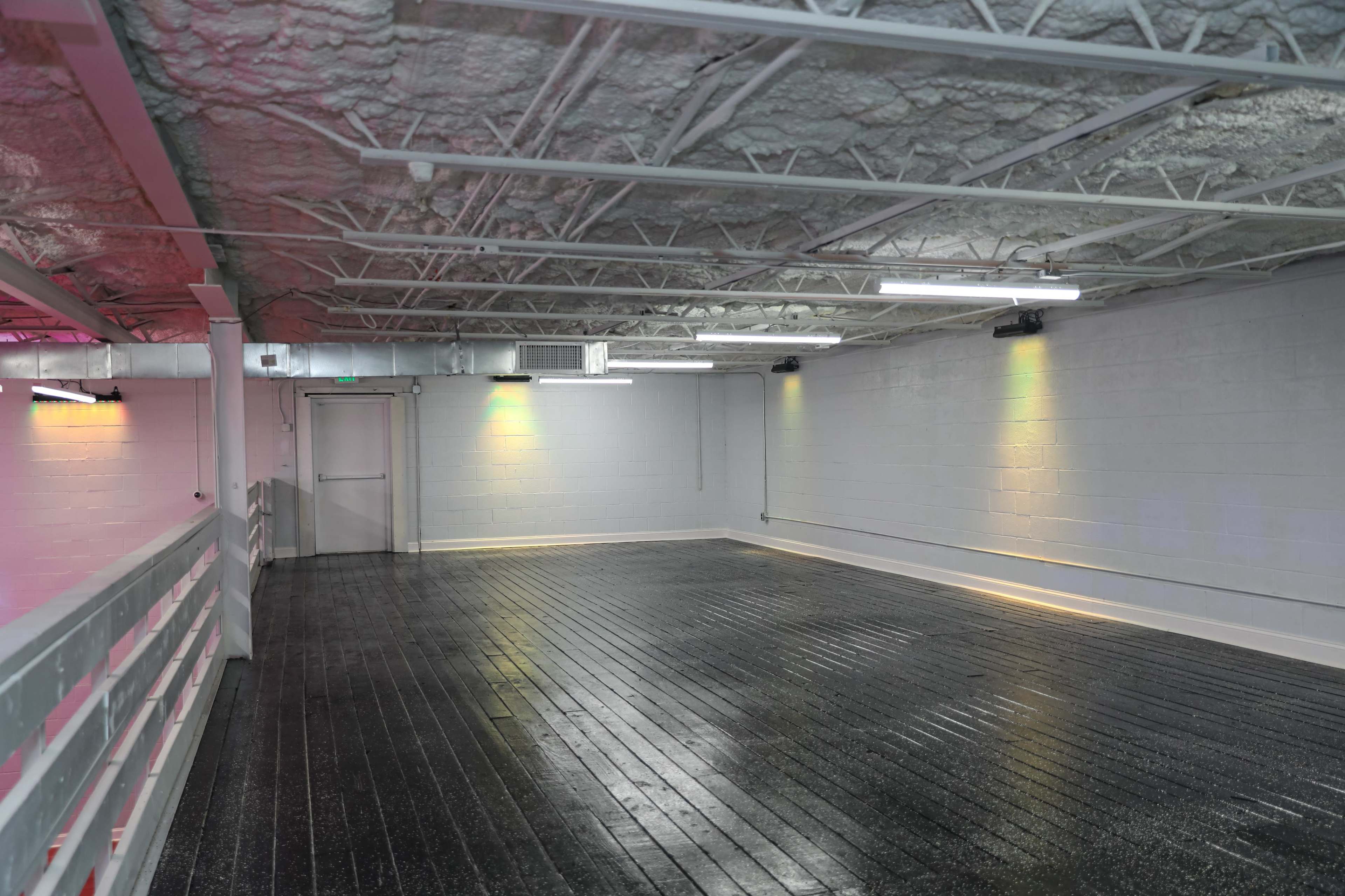 The image shows an empty indoor space with a black floor, white walls, and illuminated overhead lights.