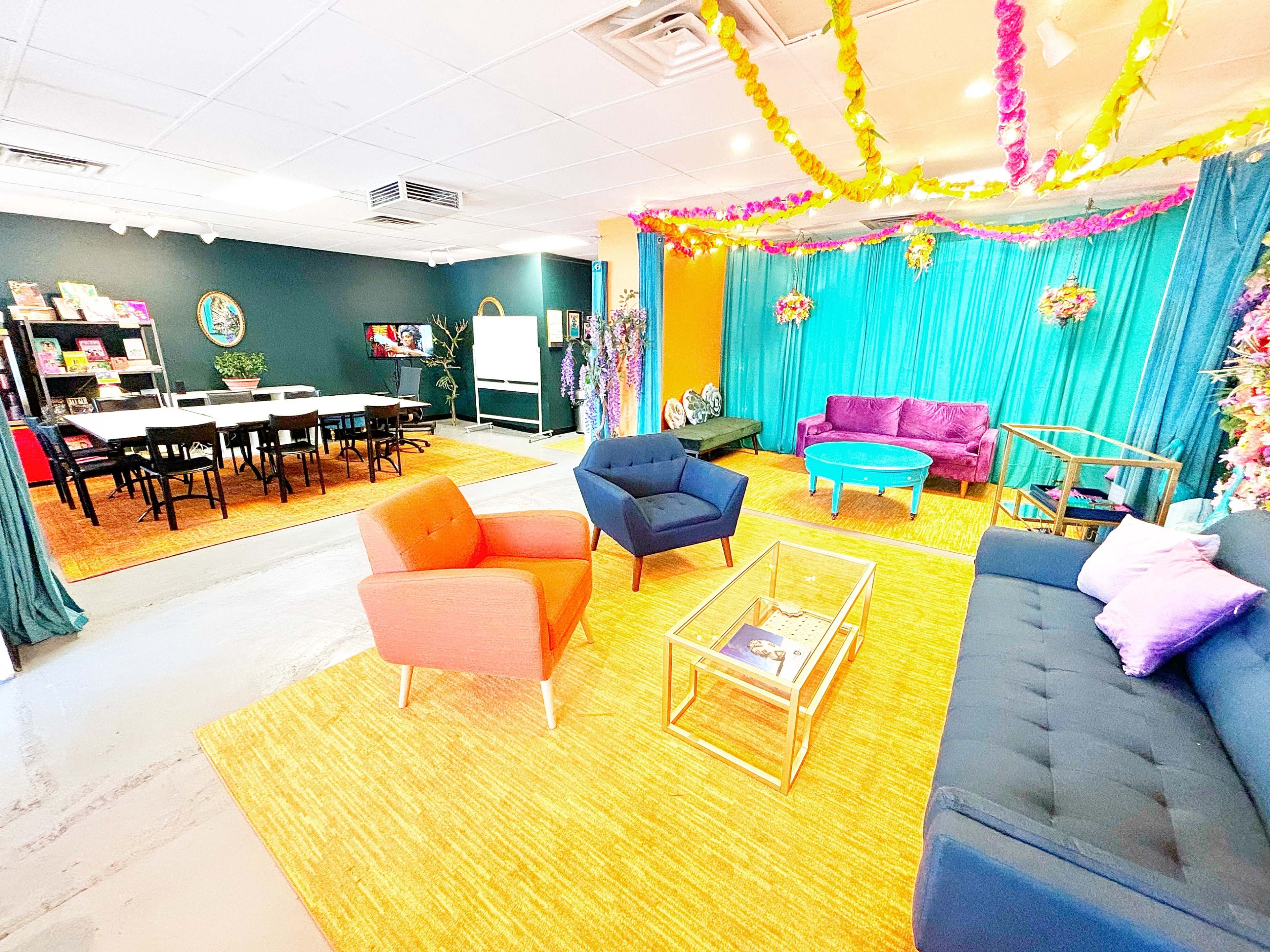 A vibrant room with colorful seating areas, a greenish-blue backdrop, and decorative elements, alongside a dining space with tables and chairs.