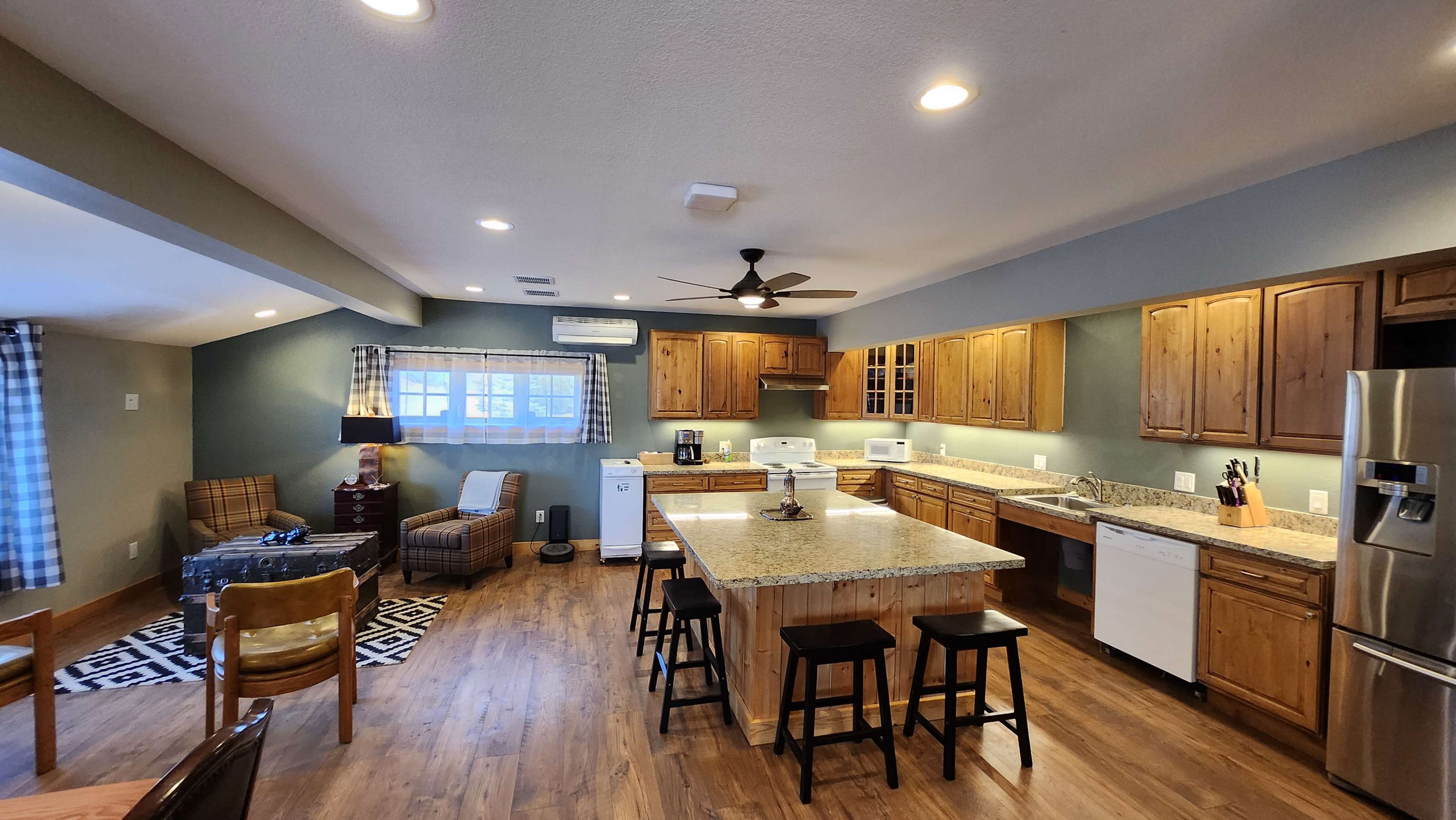 A spacious kitchen featuring wooden cabinets, a large island with a granite countertop, and modern appliances in a well-lit area.
