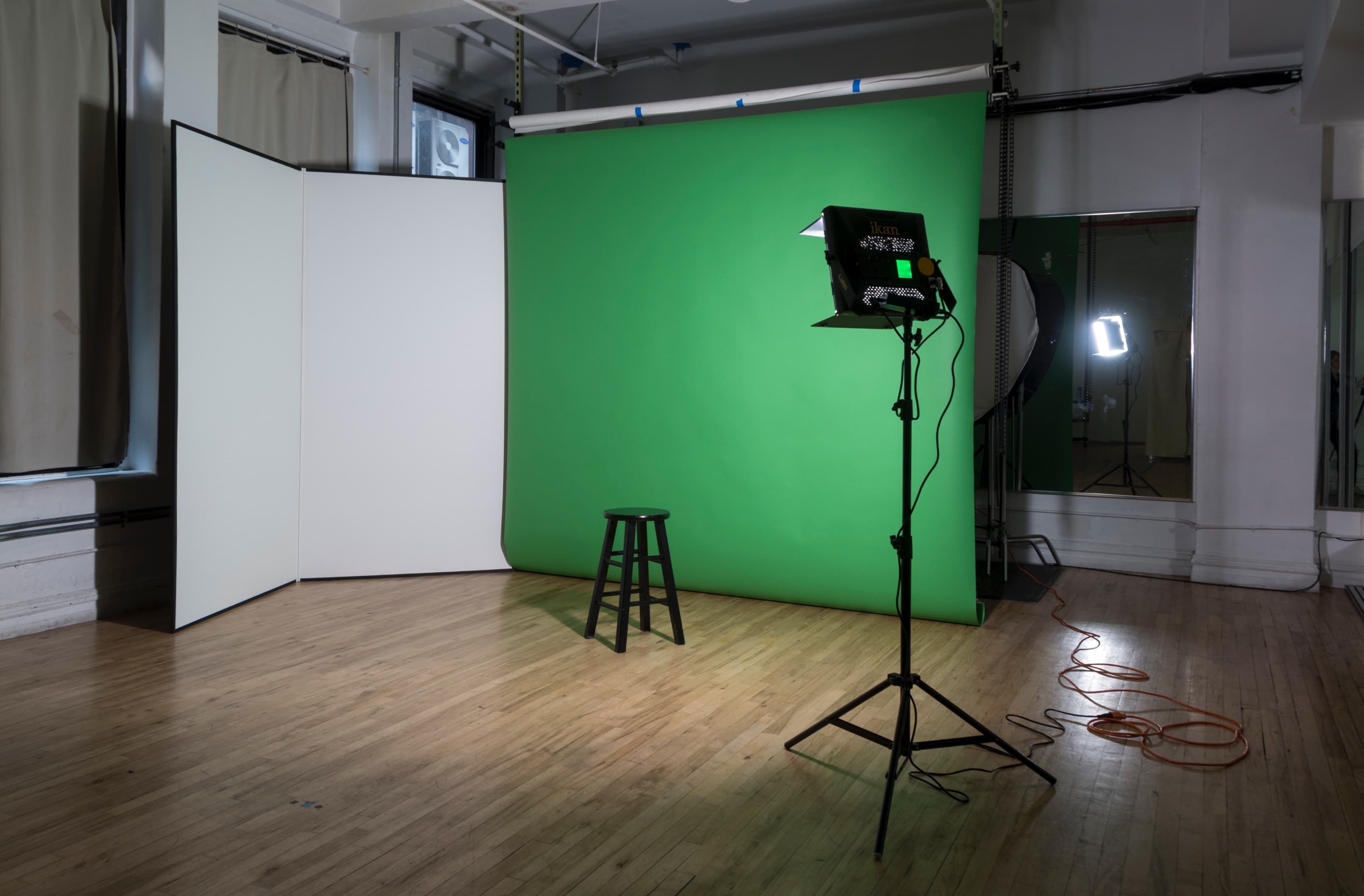 A photography studio set up with a green backdrop, a black stool, and lighting equipment.