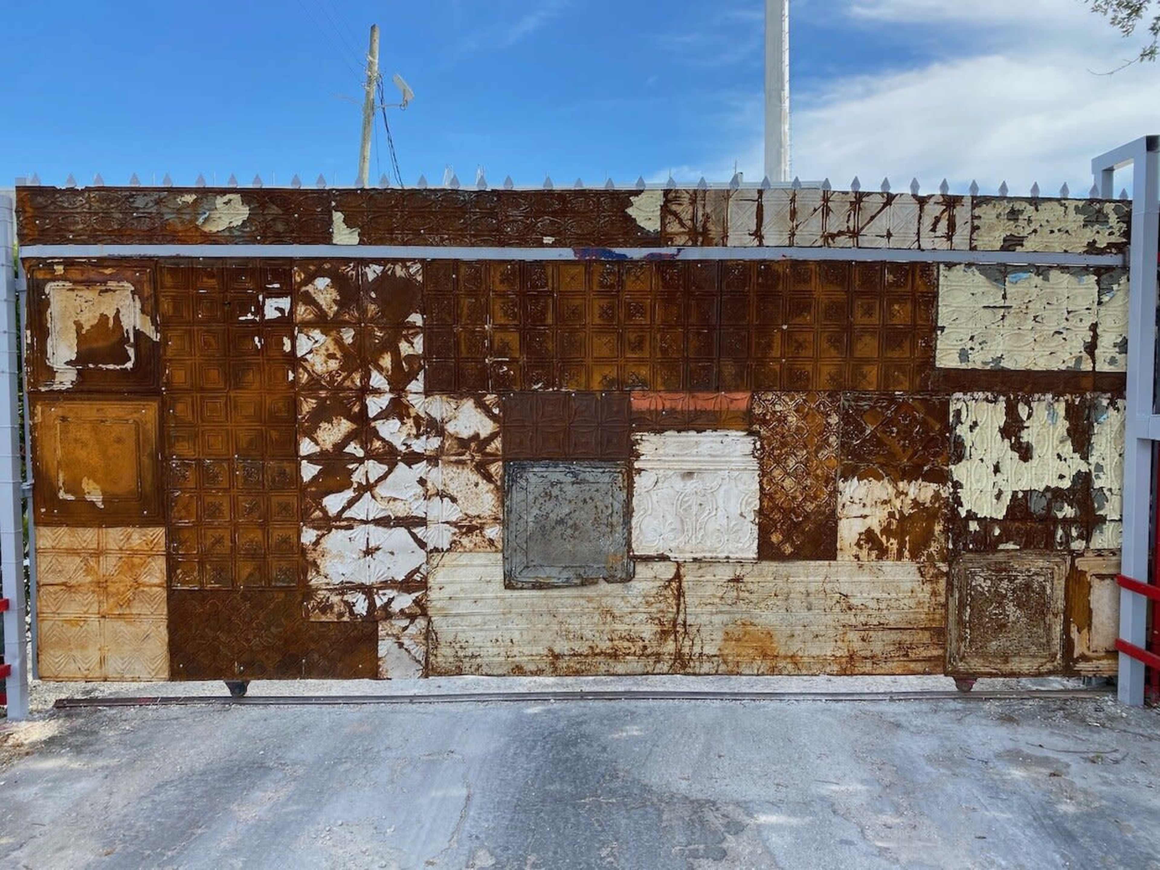 A weathered metal gate covered in rust and peeling paint features a patchwork of different textures and colors.