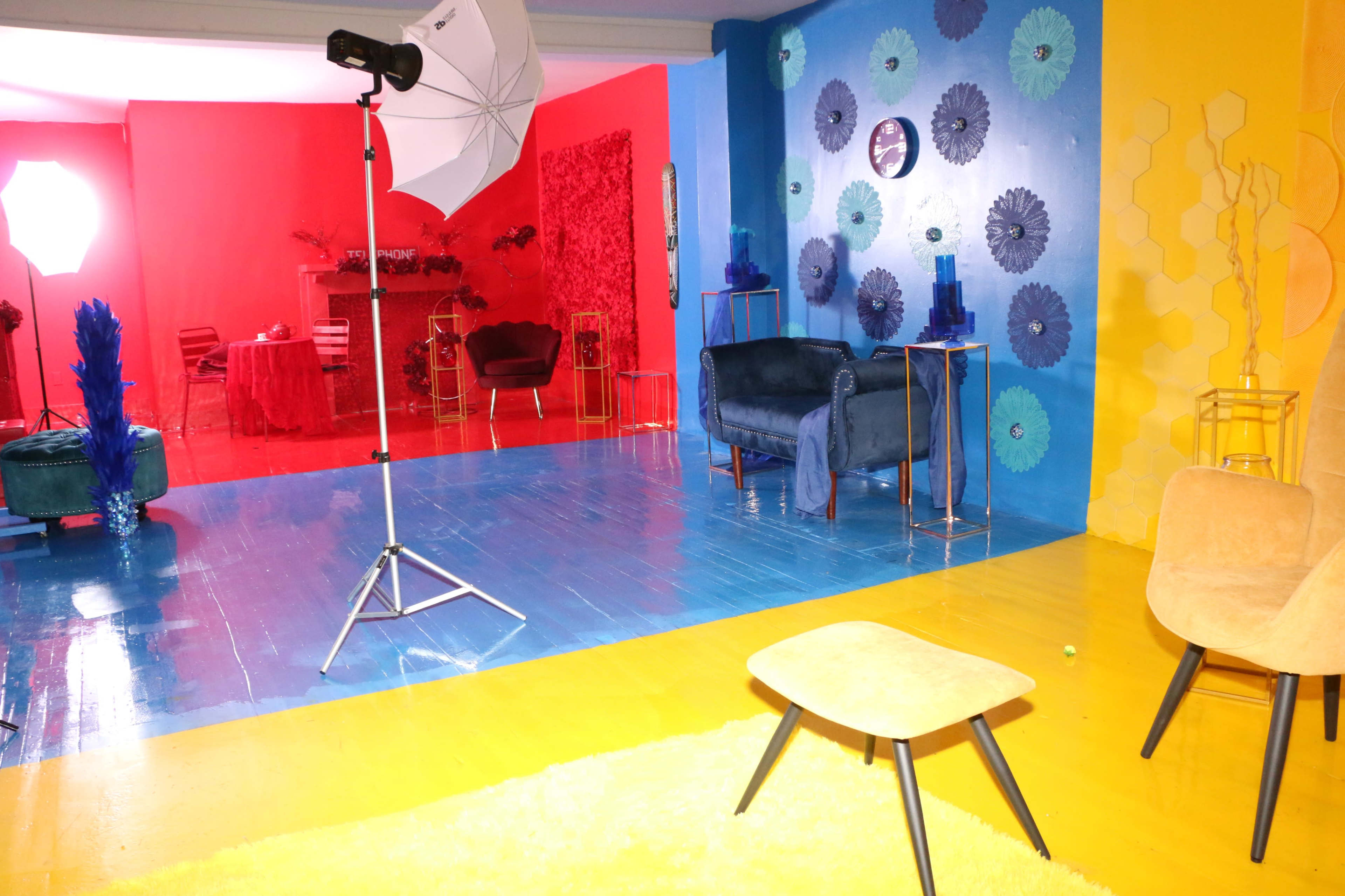 A colorful studio space features a blue and yellow floor, styled furniture, and varying backdrop decorations in red and blue.