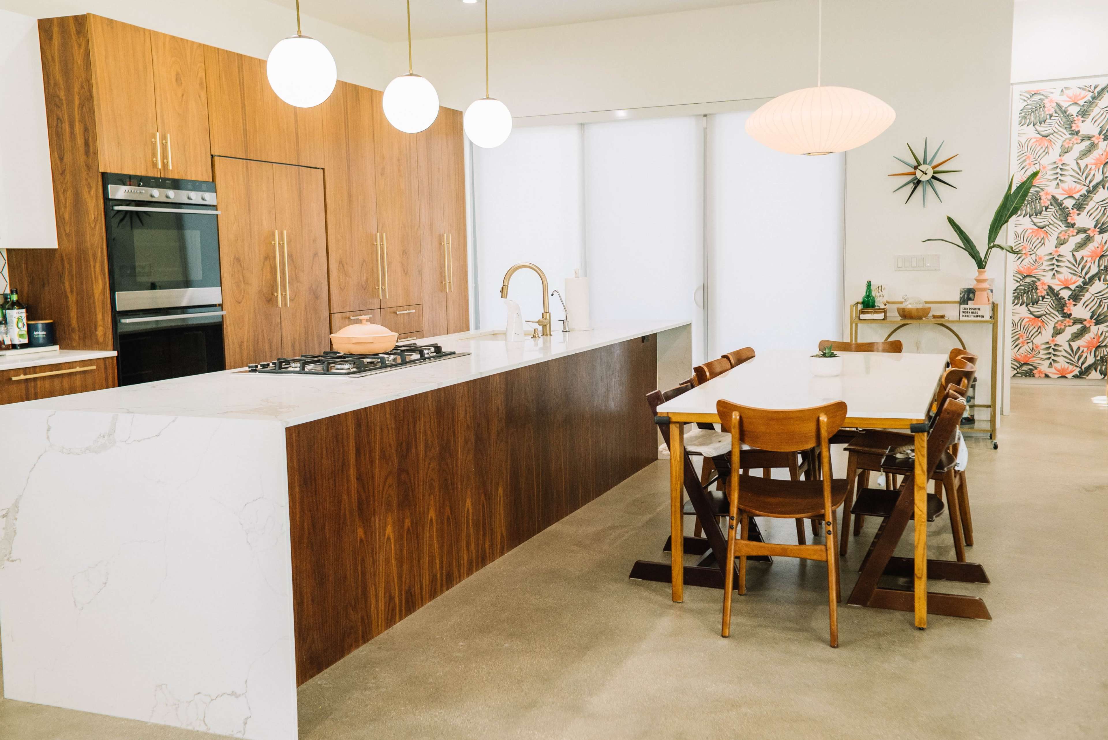 A modern kitchen with wooden cabinetry, a marble countertop, and a dining table surrounded by wooden chairs.