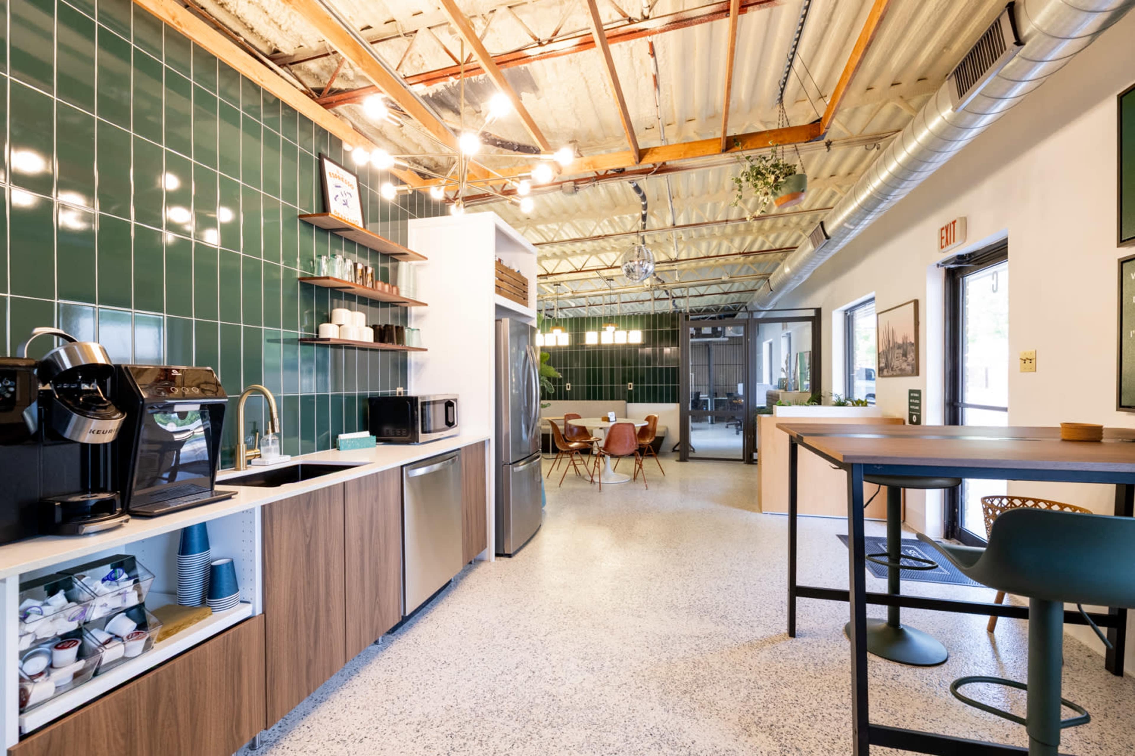 The image shows a modern kitchen area with green tiles, stainless steel appliances, and a dining space visible in the background.