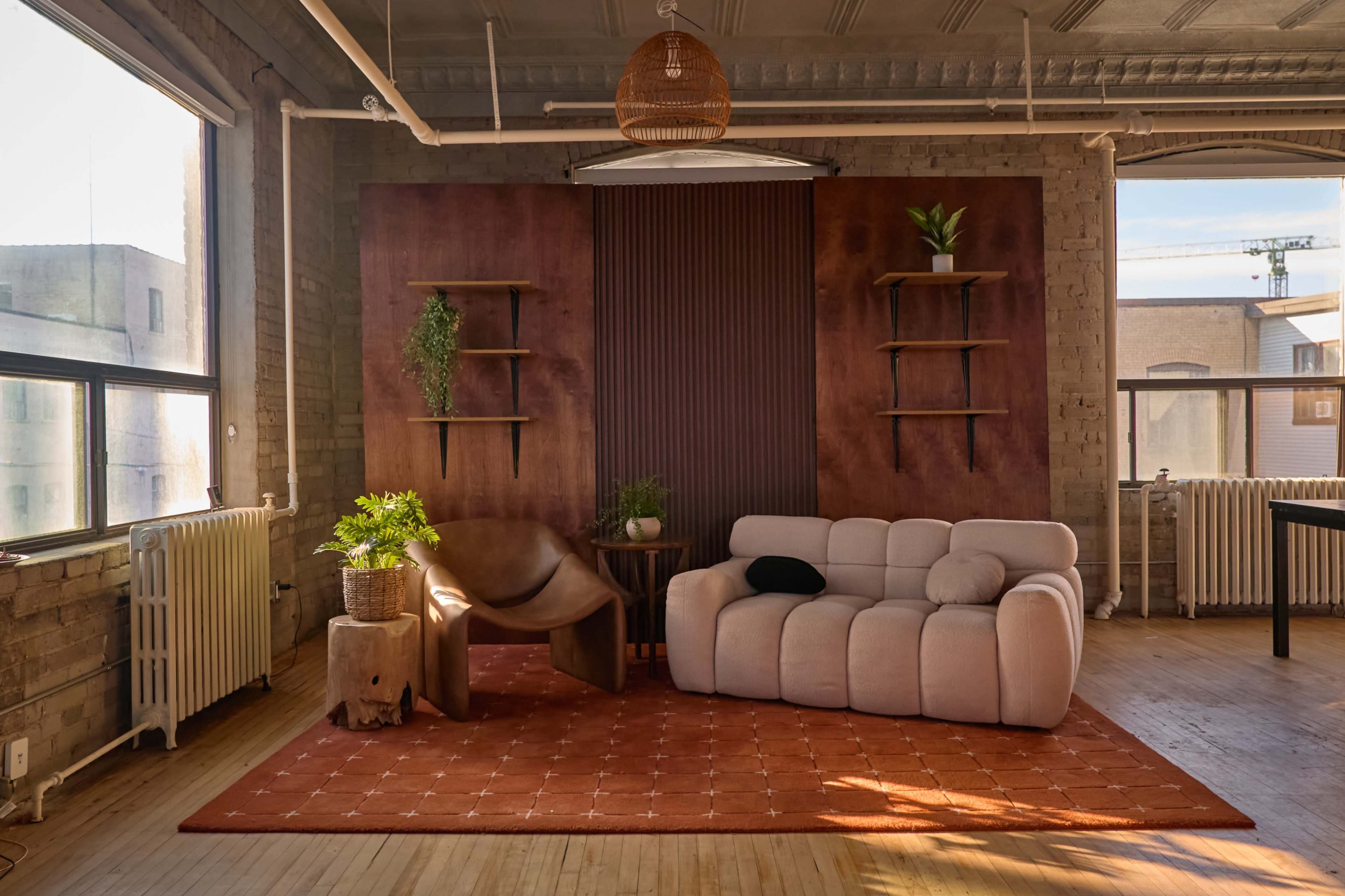 The image shows a modern living space with a plush sofa, a wooden side table, and decorative plants against a textured wall.