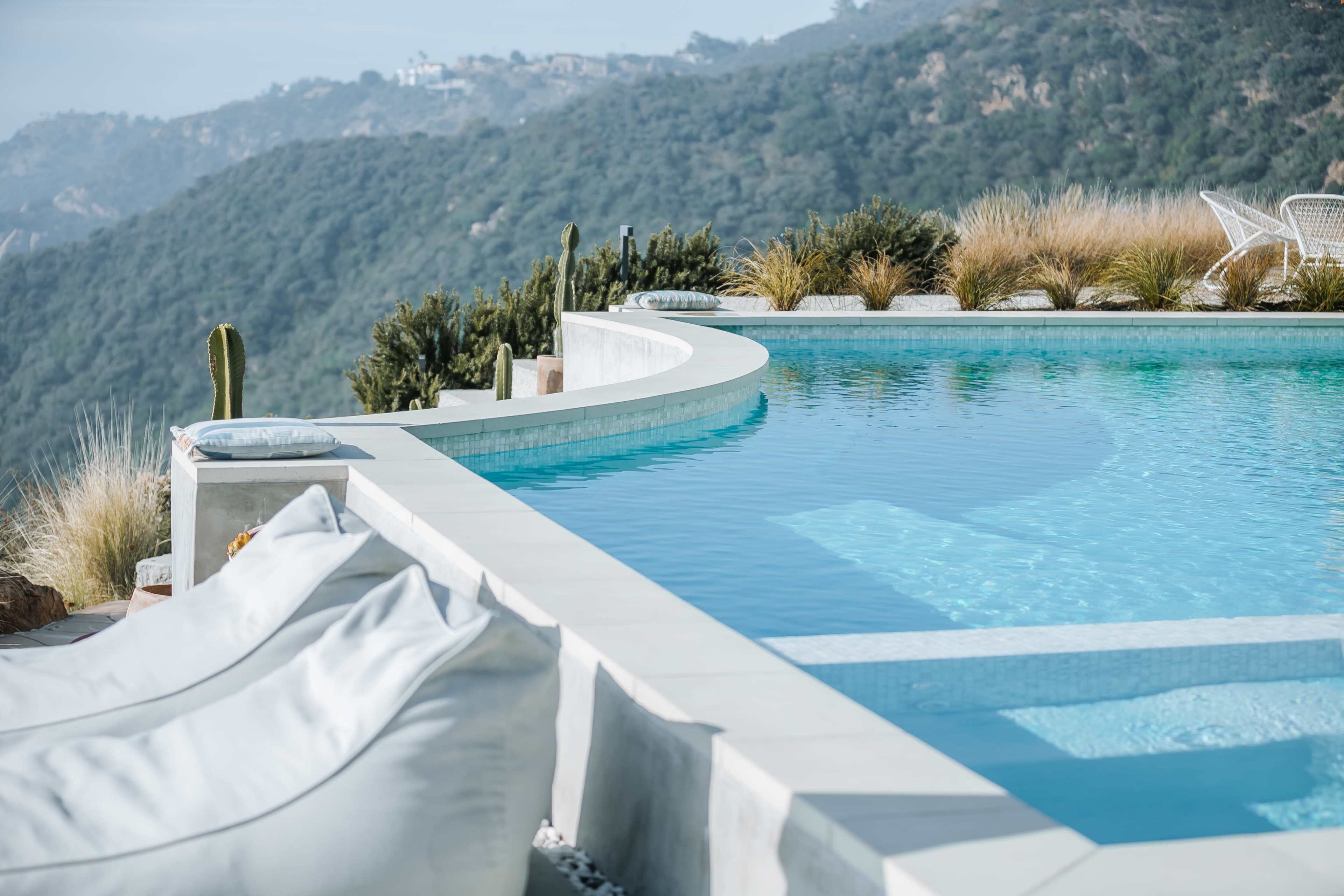 A modern infinity pool overlooking a mountainous landscape, with lounge chairs and desert vegetation nearby.