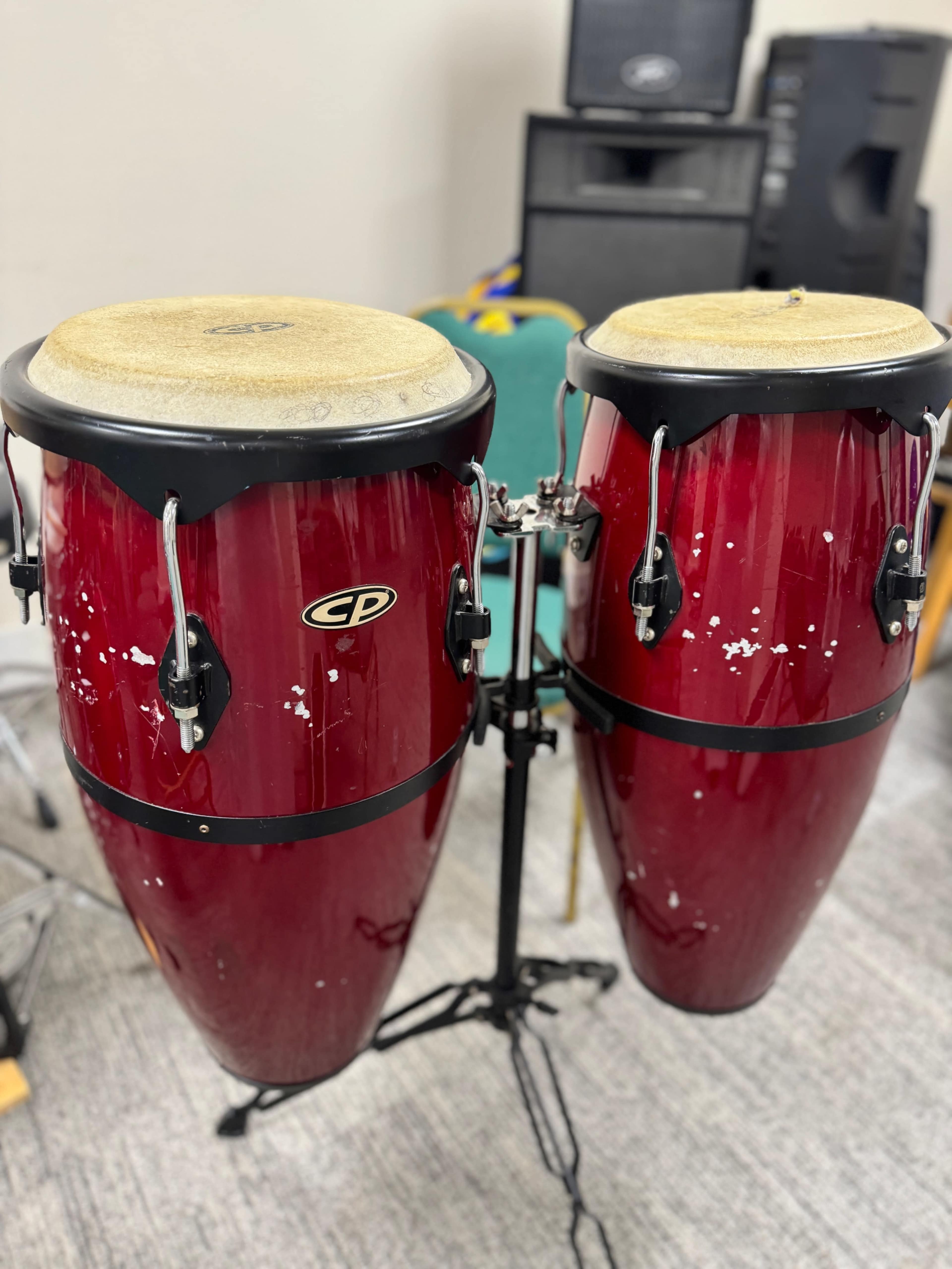 A pair of red conga drums mounted on a black stand in a music rehearsal space.