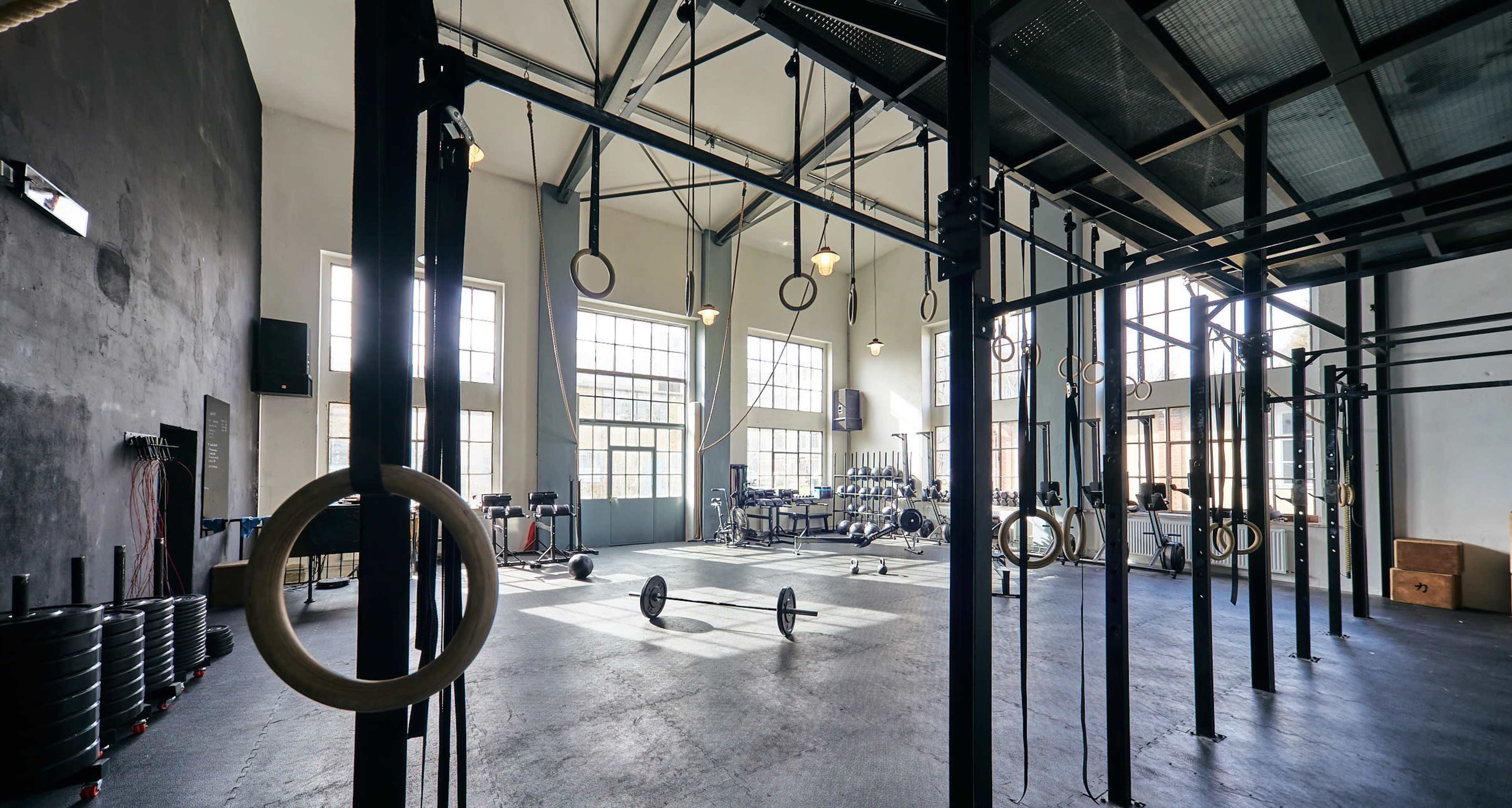 A spacious gym with high ceilings, several workout stations, and Olympic rings hanging from a structure.