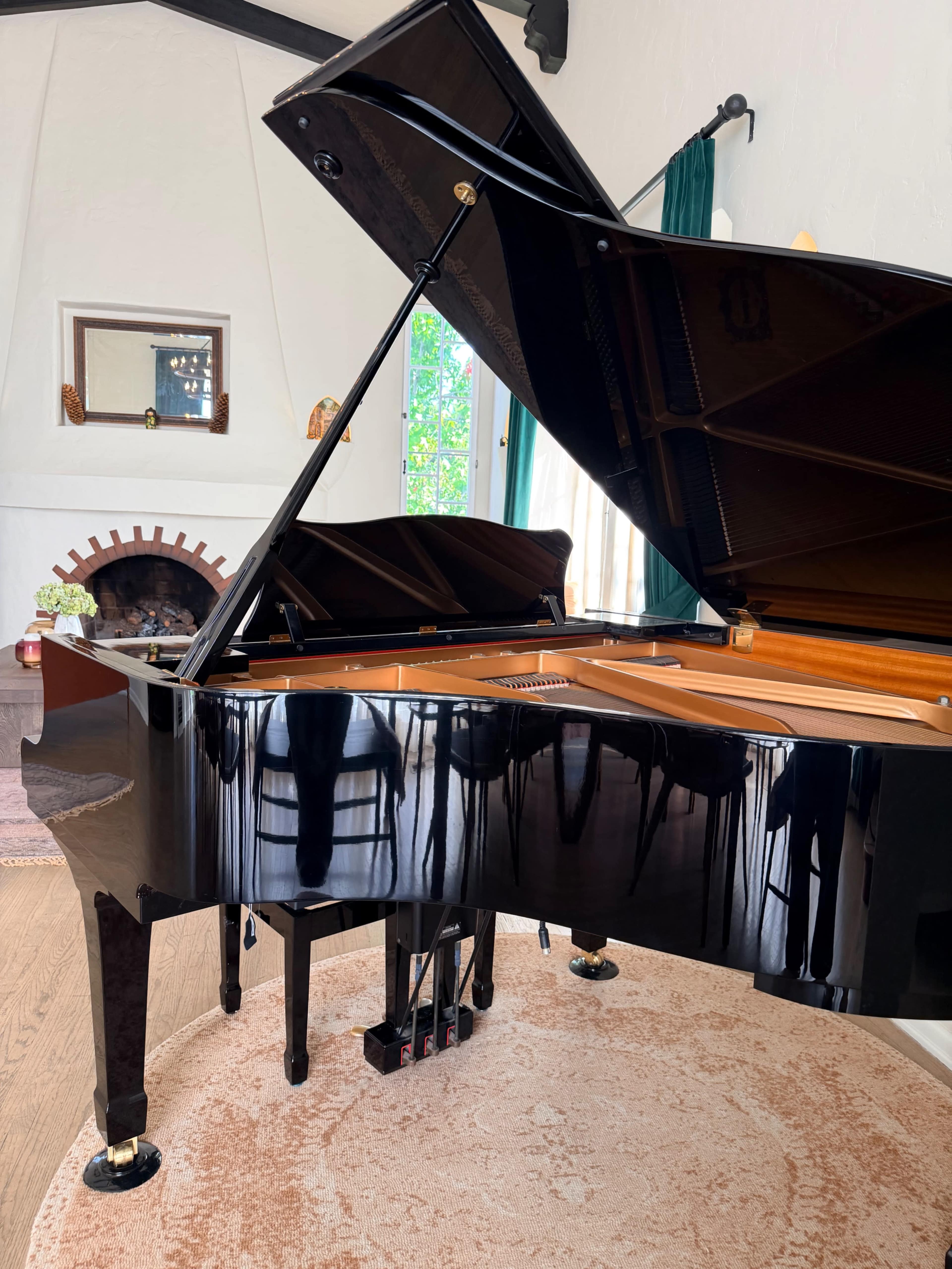The image shows a grand piano positioned in a bright room with a fireplace and large windows.