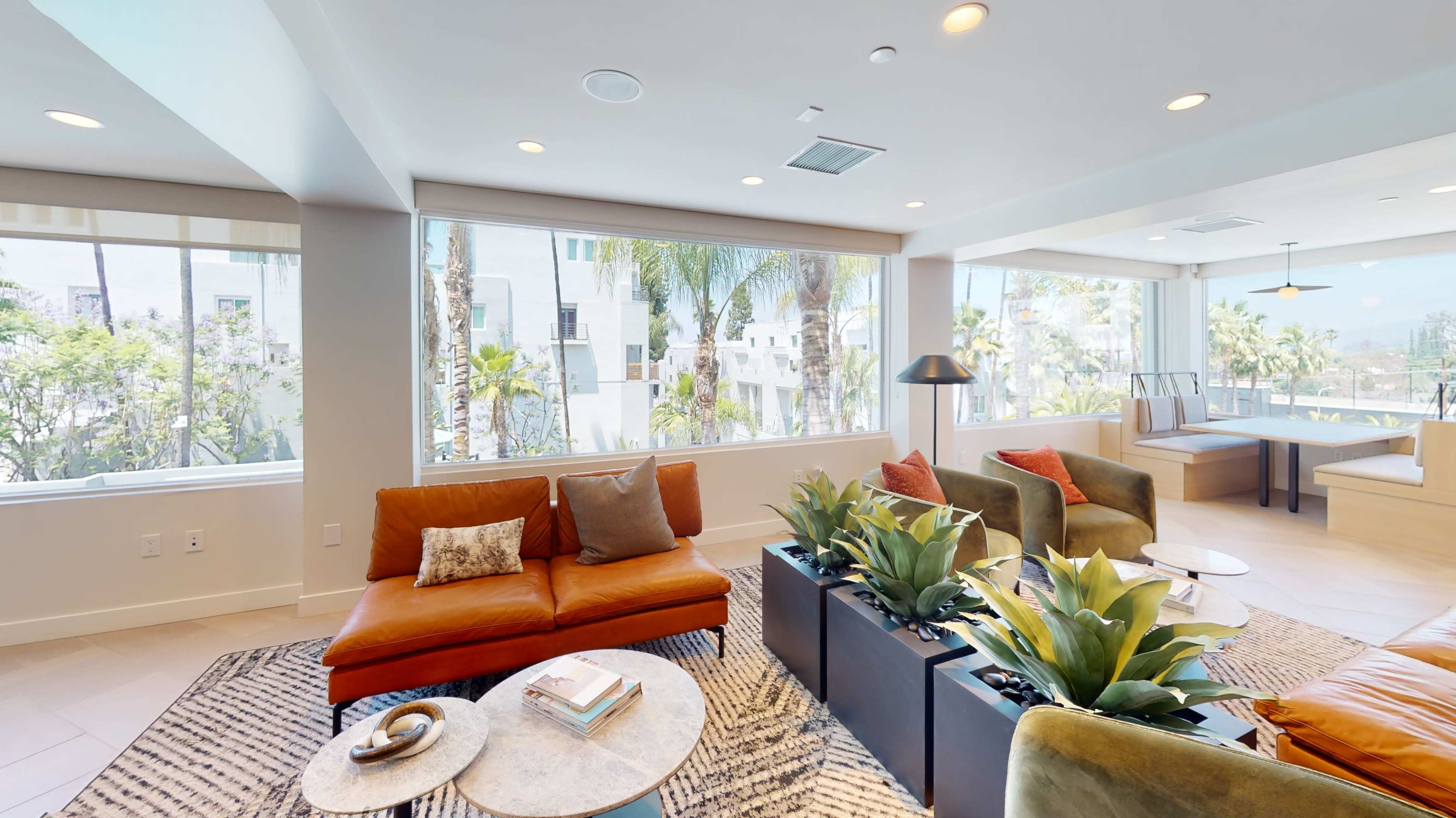 A modern living area with large windows, a brown leather sofa, decorative plants, and a coffee table.