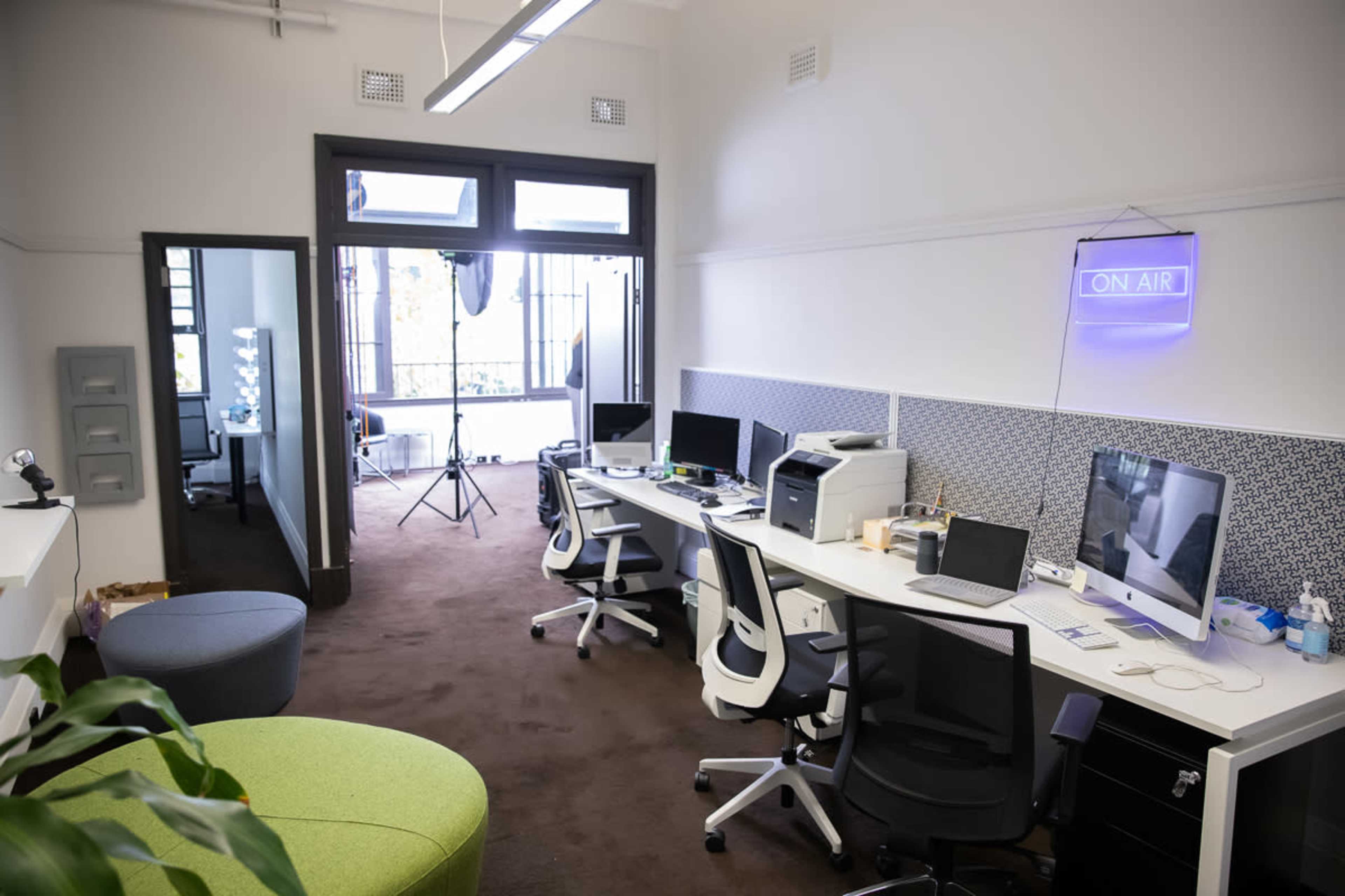 A modern office space with multiple desks, computers, and a green seating area.
