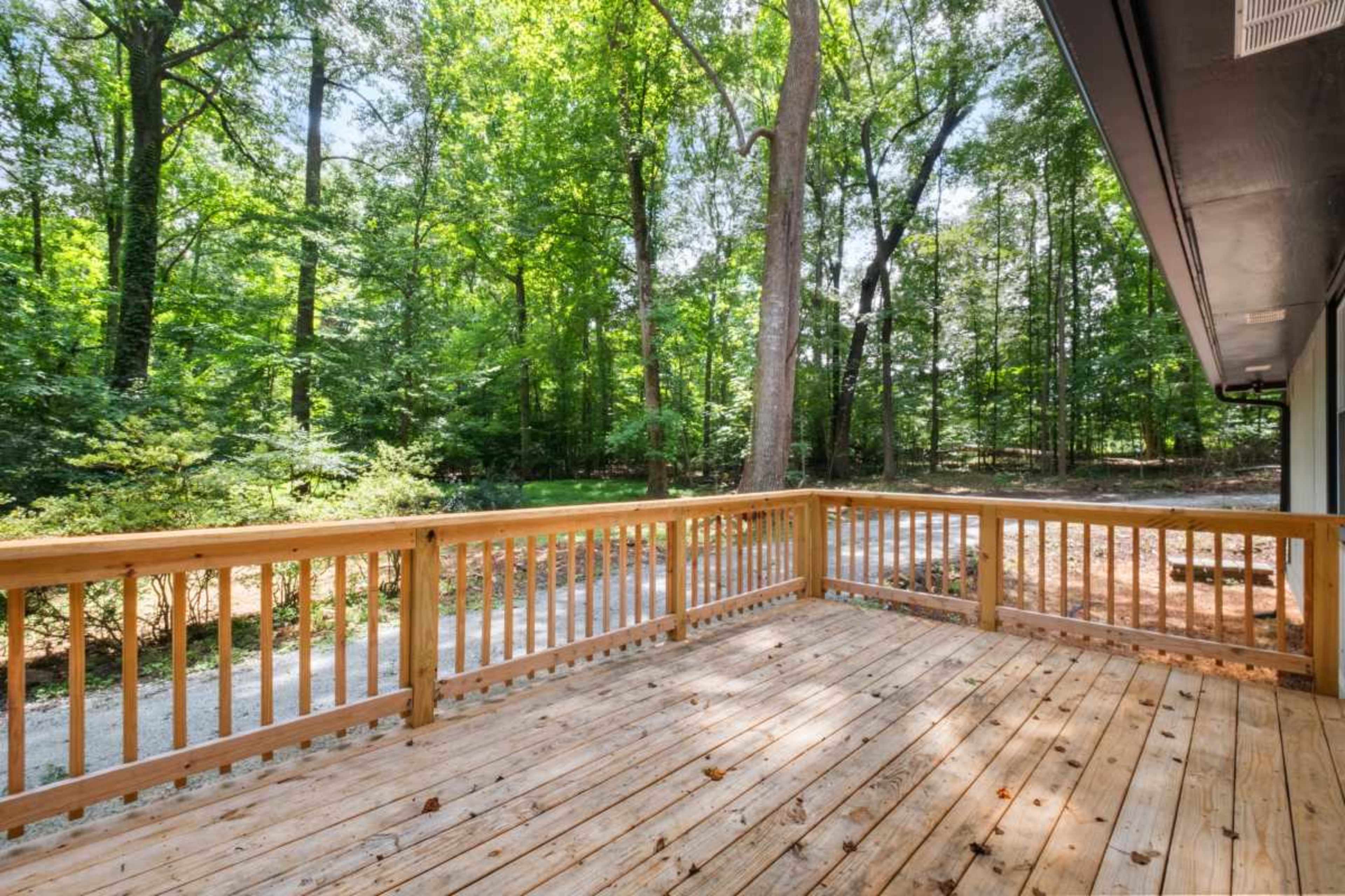 A wooden deck with a railing overlooks a dense, green forest.