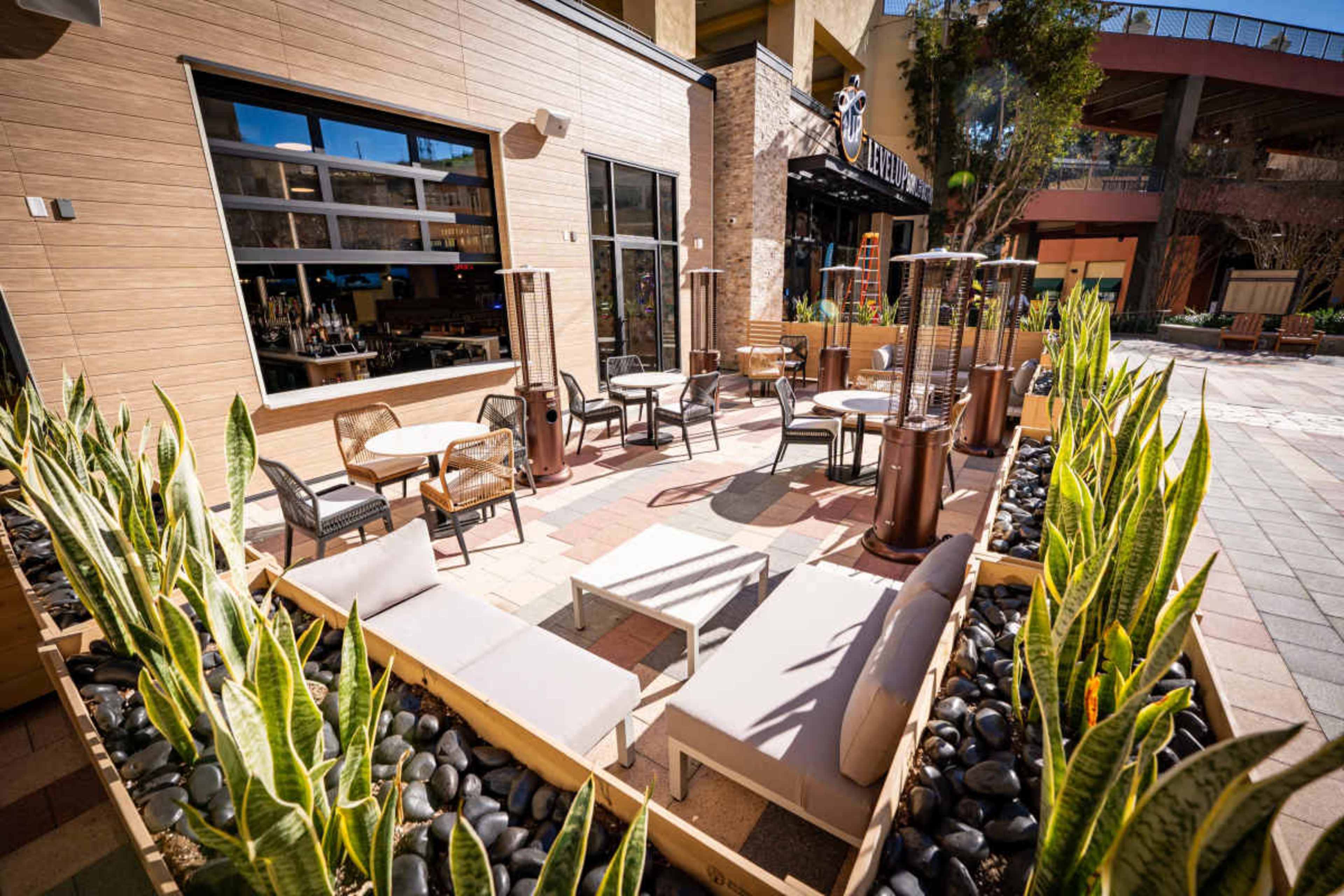 The image shows an outdoor seating area of a restaurant with tables, chairs, and planters containing plants and decorative stones.