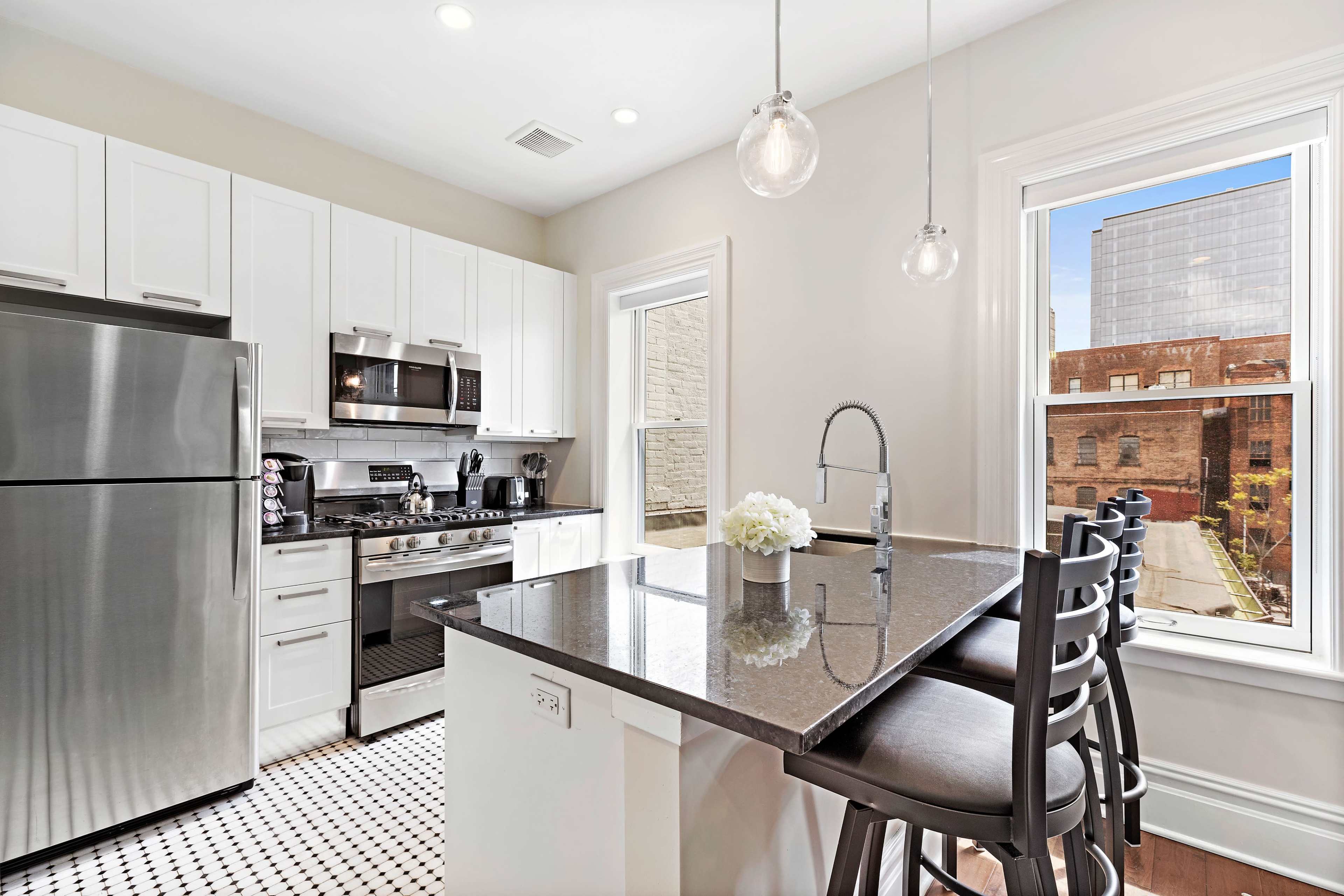 A modern kitchen features stainless steel appliances, white cabinetry, and a dark granite island with seating.