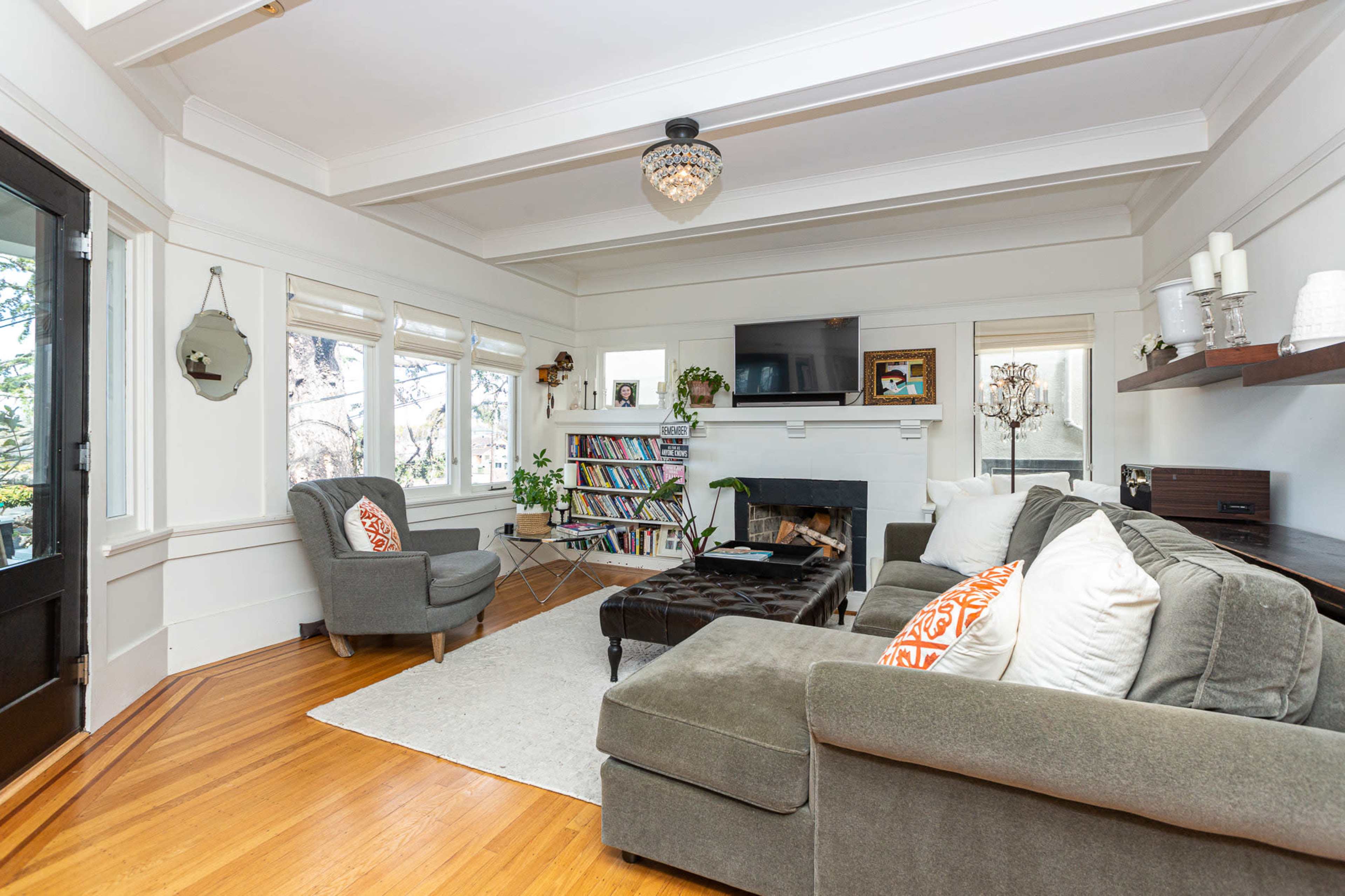 The living room features a comfortable seating area with a plush sofa and armchairs, a flat-screen TV mounted above a fireplace, and a bookshelf filled with books.