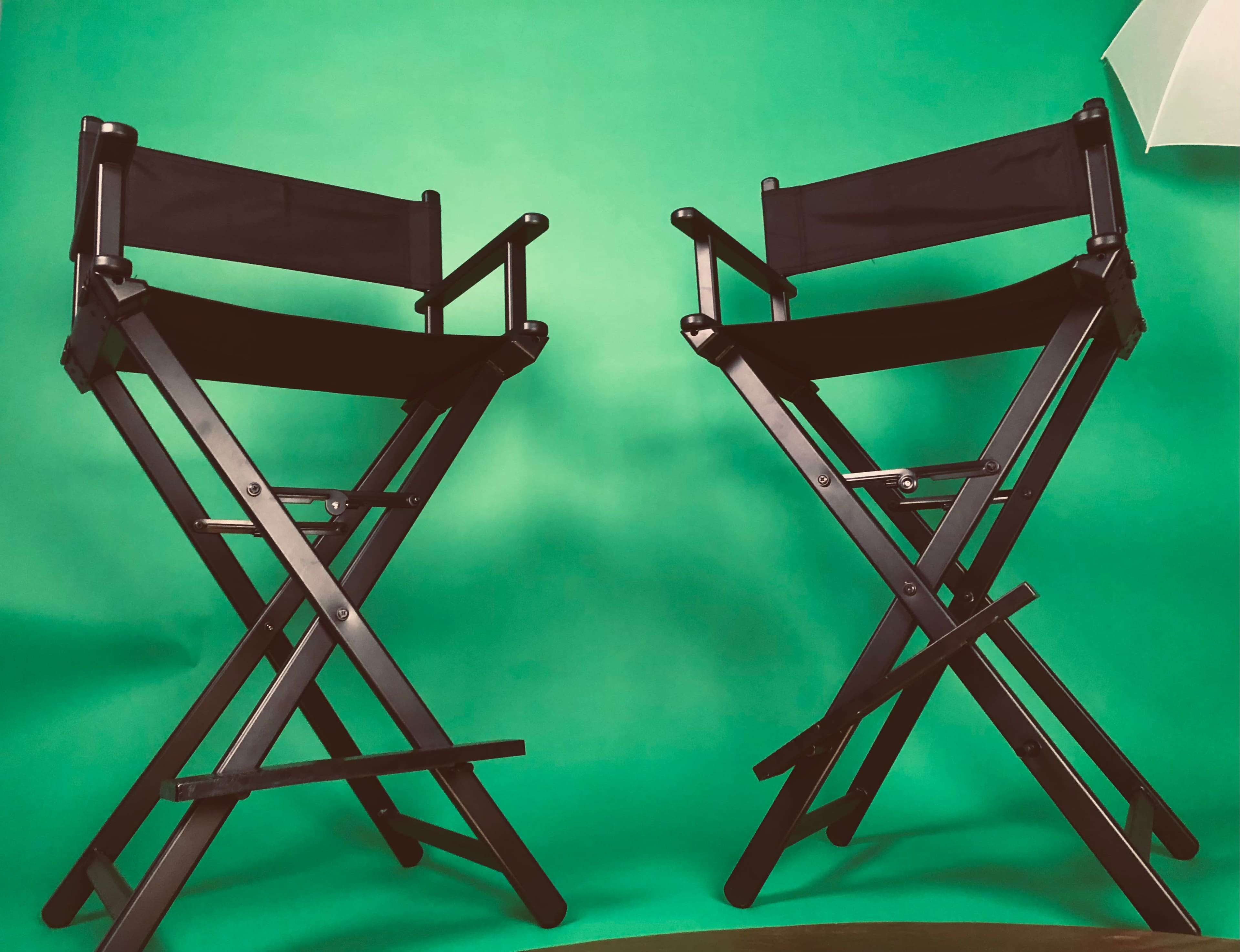 Two black folding director's chairs are positioned in front of a green backdrop.