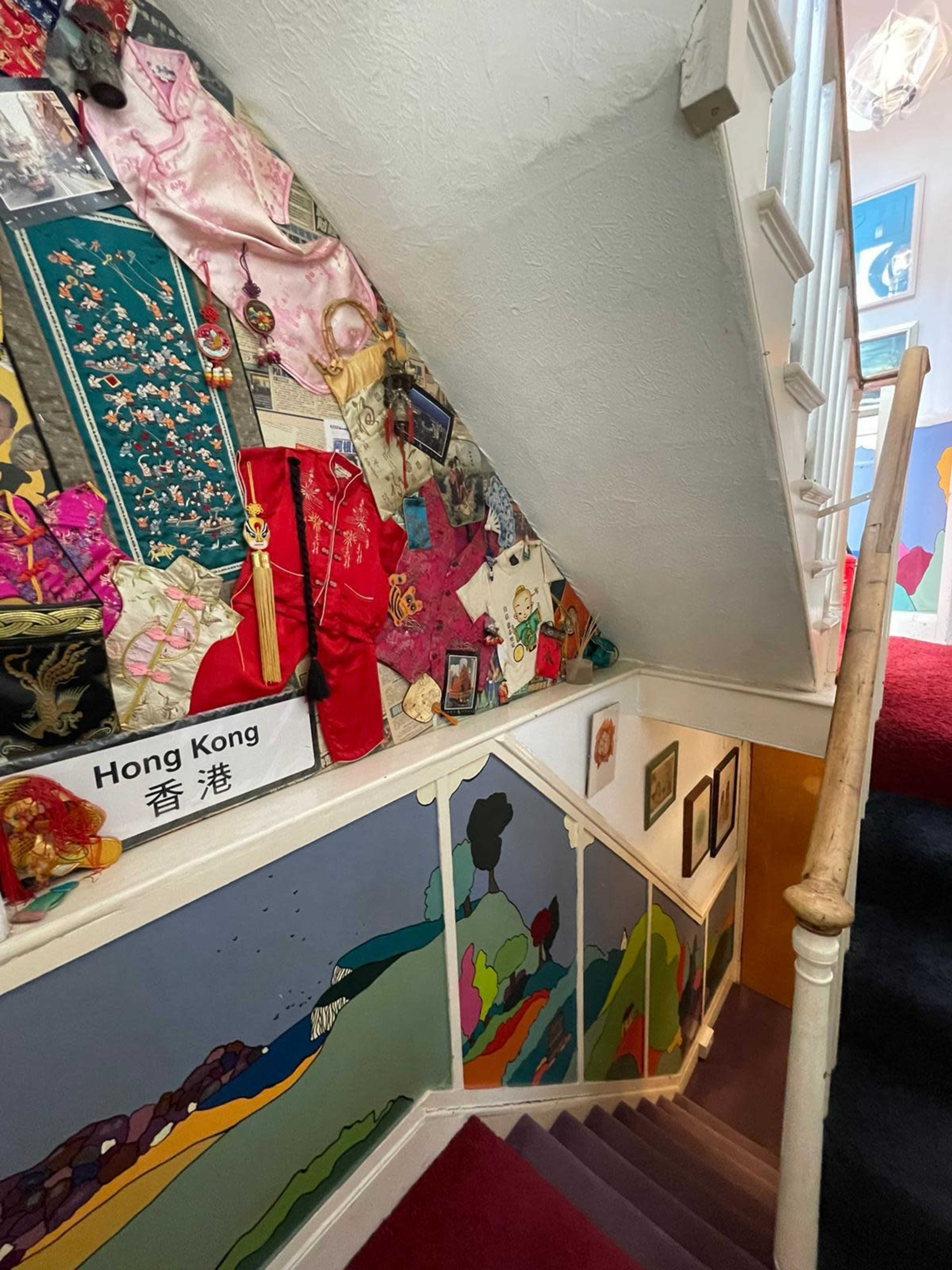 The image shows a staircase adorned with colorful fabric and artwork, leading to an upper floor.