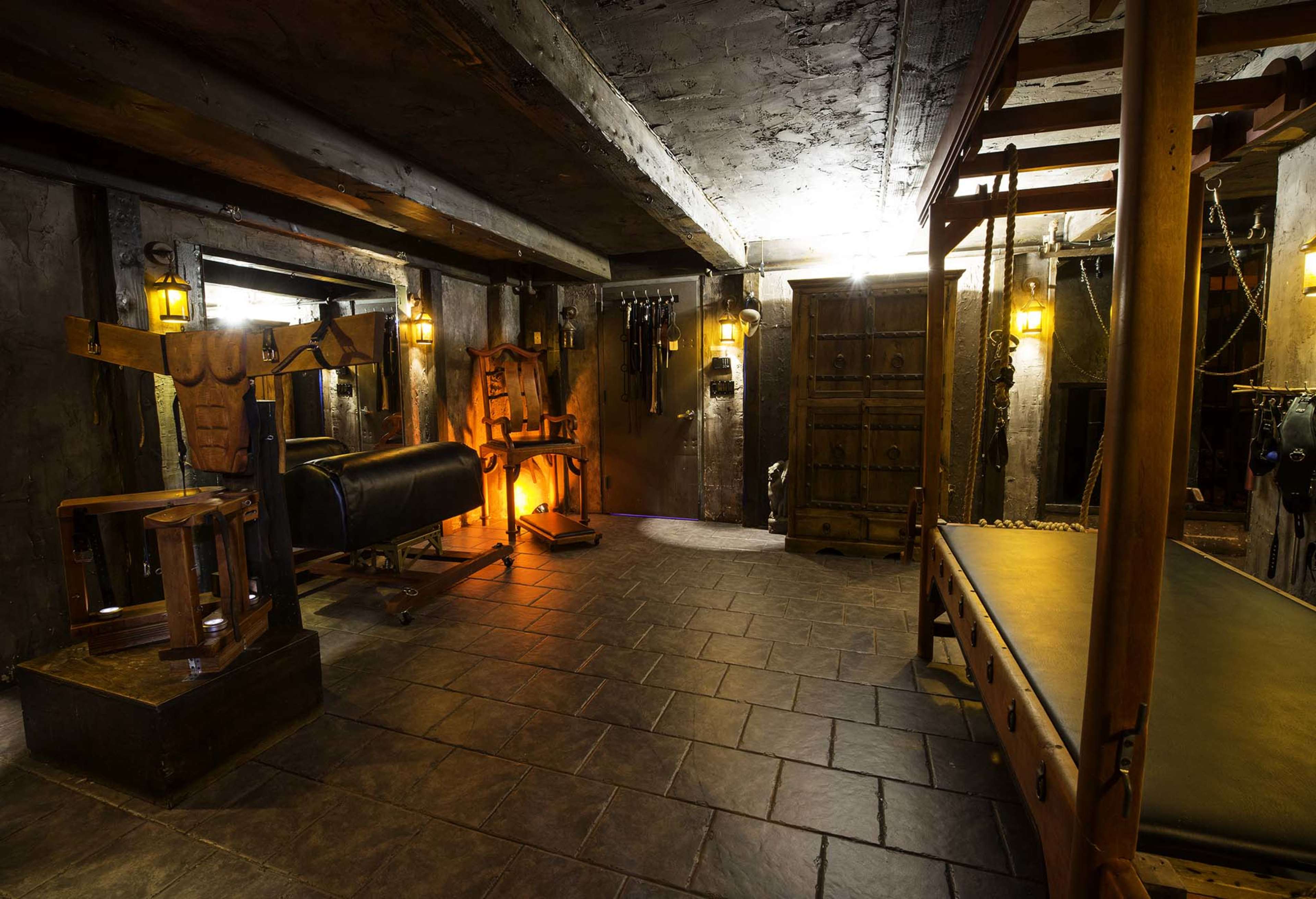 The image shows a dimly lit underground room with stone walls, featuring various pieces of exercise equipment and a wooden bench.