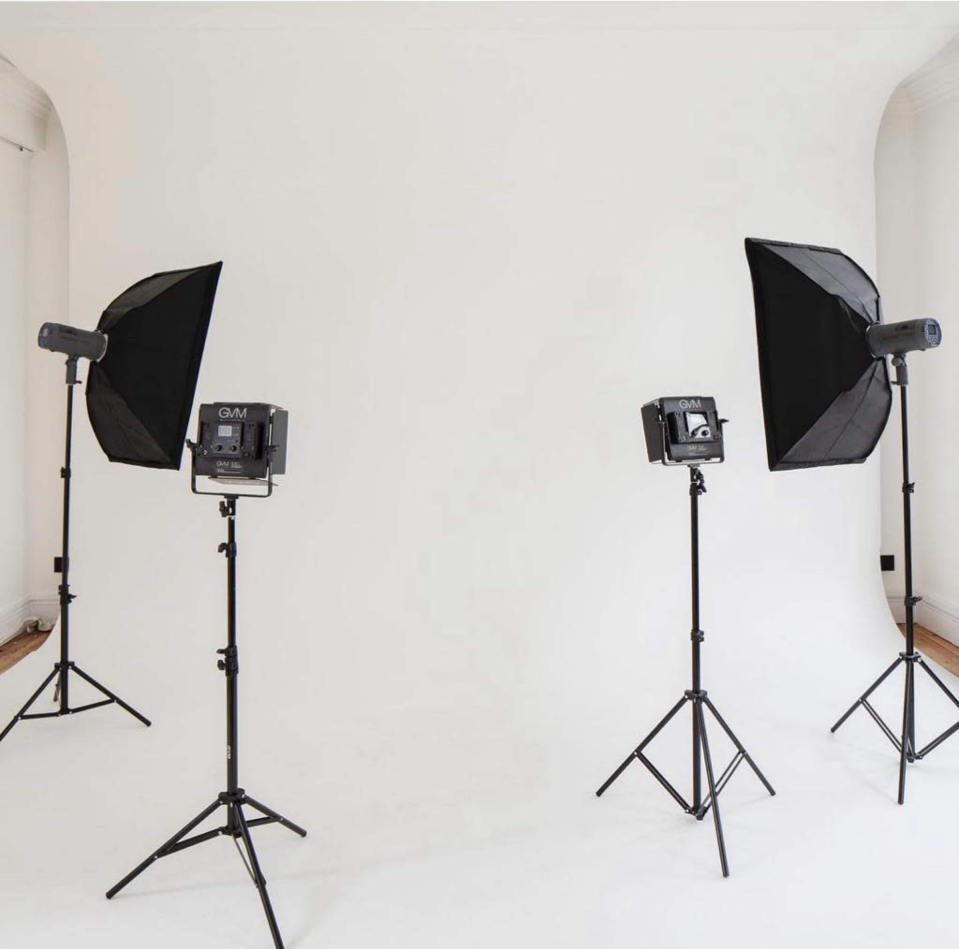 A photography setup with four light stands and softbox lights arranged in front of a white backdrop.