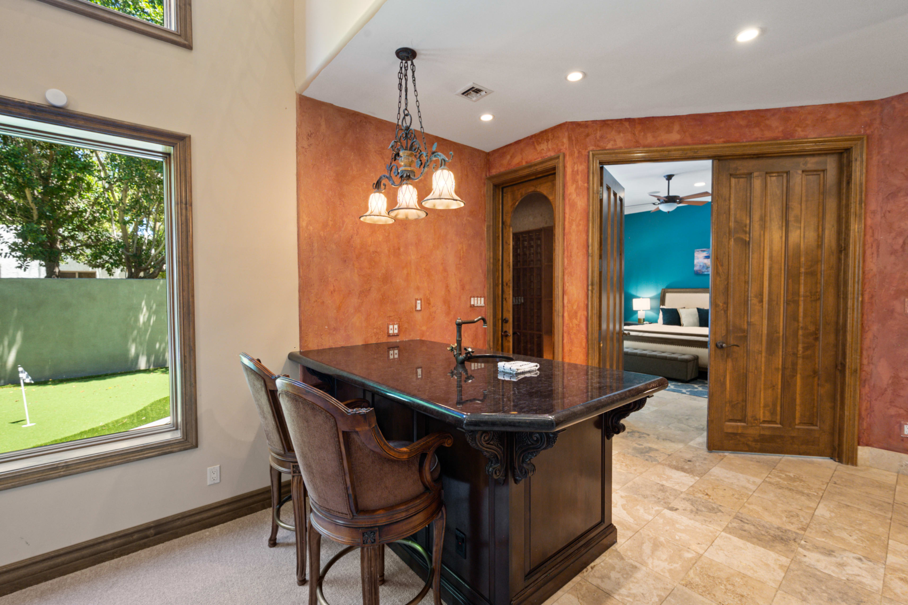 The image shows a room with a wooden bar counter, three high-backed chairs, and an arched doorway leading to a blue-painted bedroom.