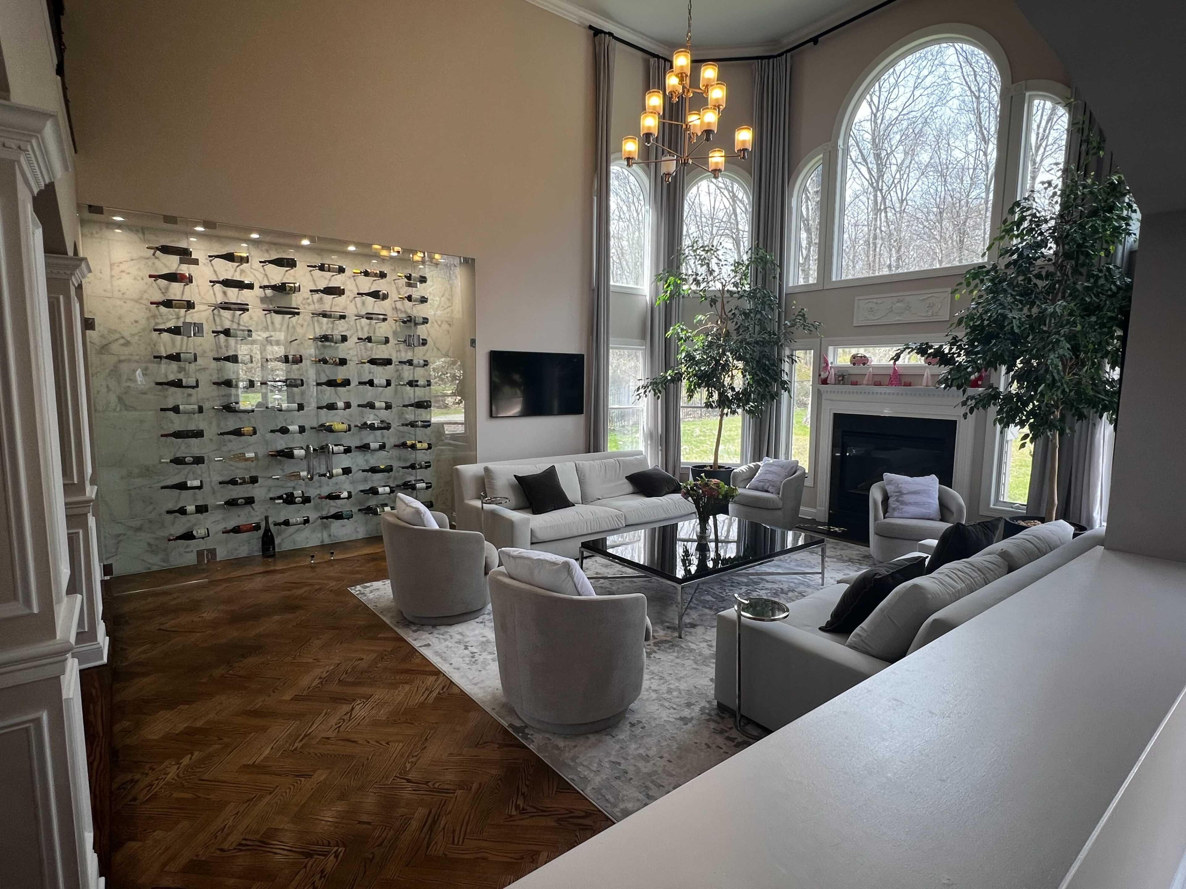A modern living room features a glass wine display, large windows, and comfortable seating arrangements.