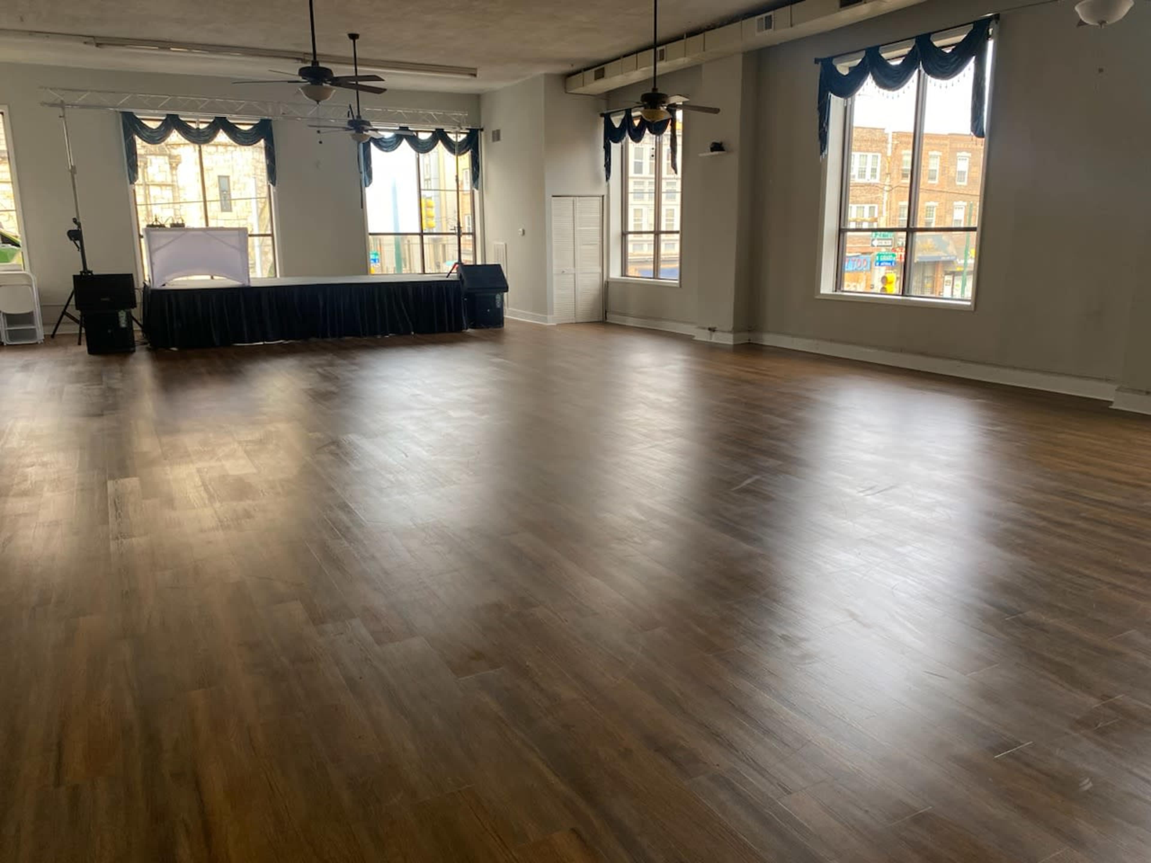 A spacious room with wooden flooring, large windows, and a stage set against the back wall.