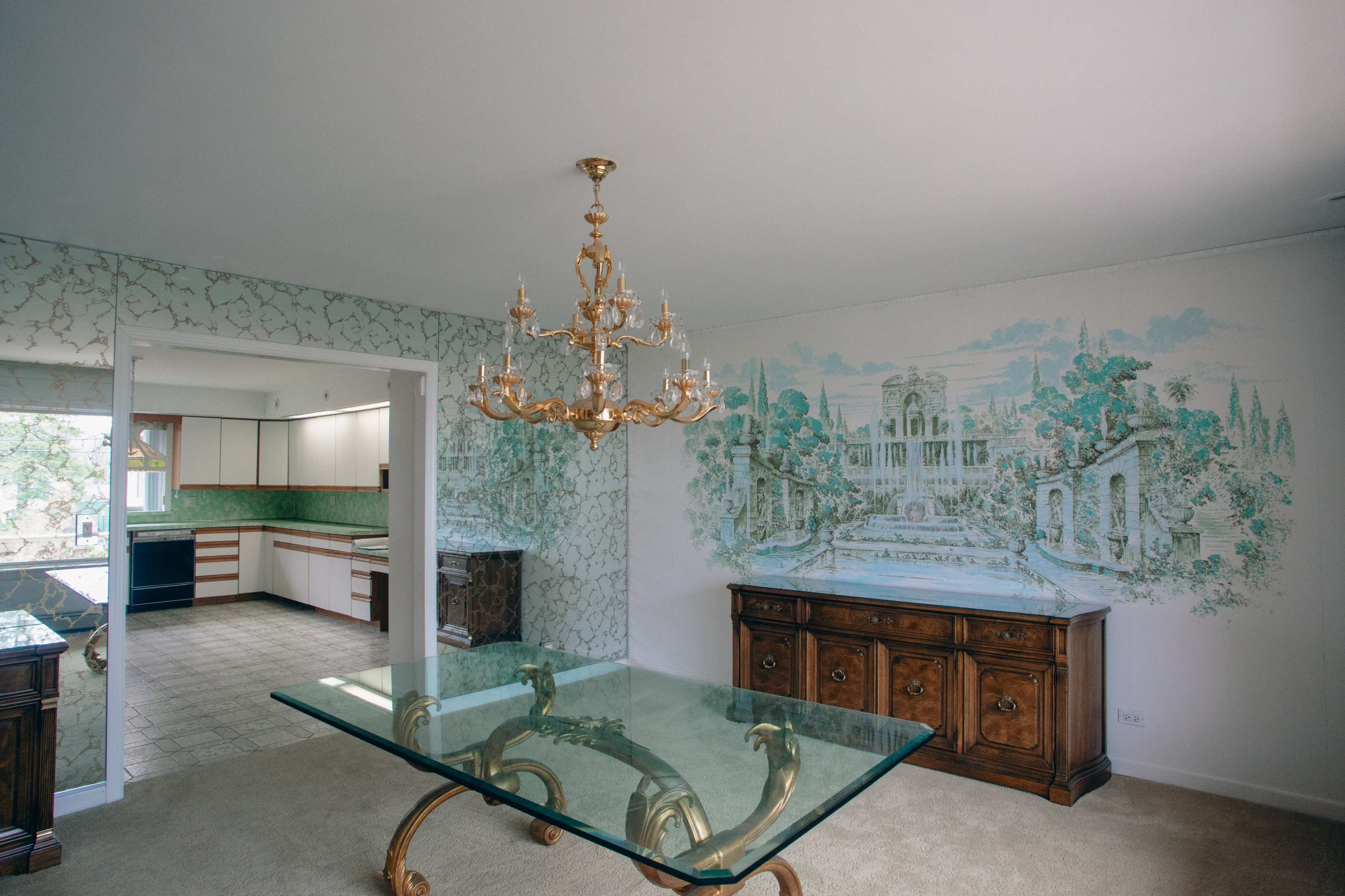 A dining area features a glass table with a golden chandelier and a mural depicting a garden scene on one wall.