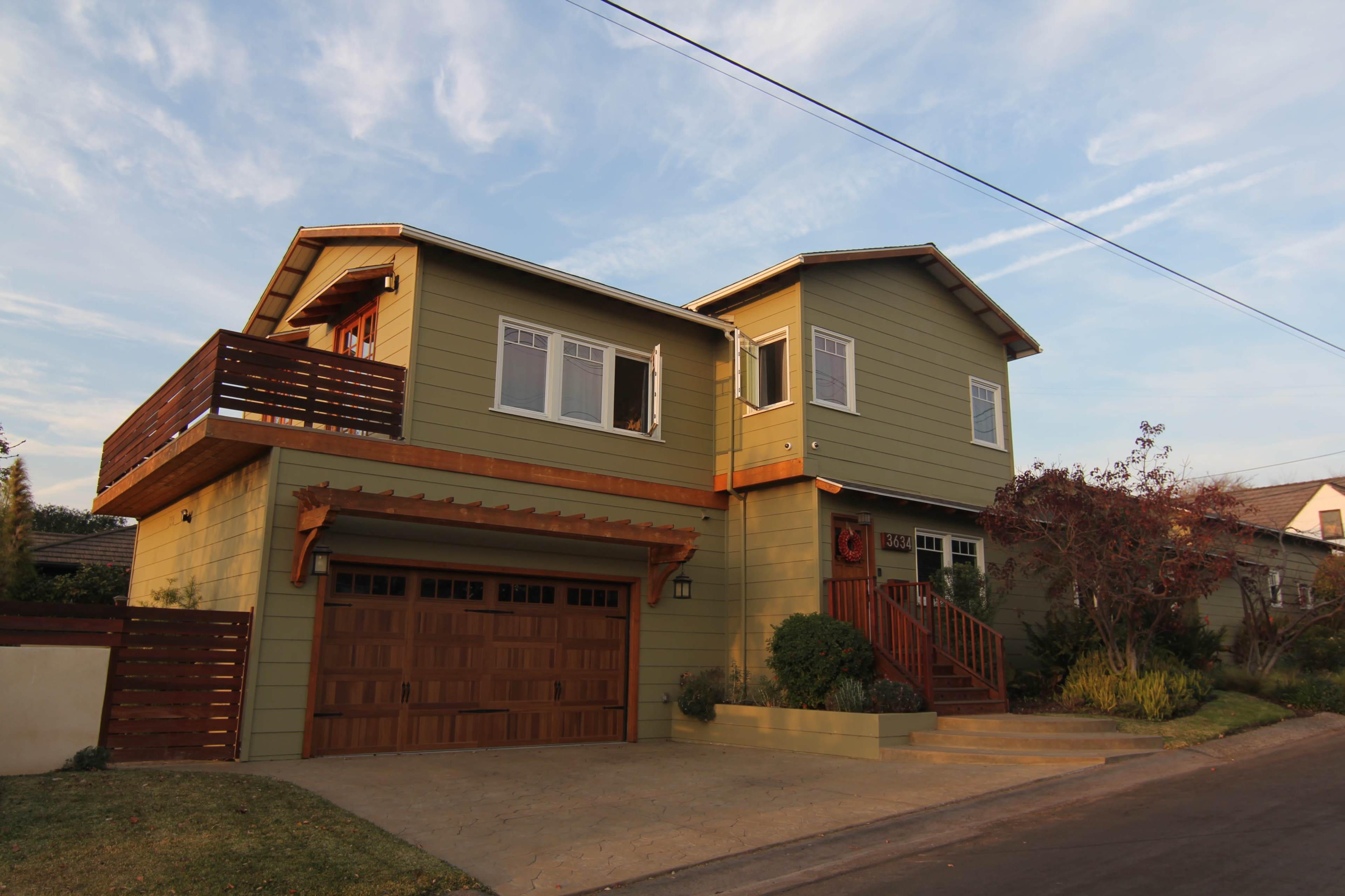 A two-story green house with a wooden garage door and a small front porch, surrounded by a neatly landscaped yard.