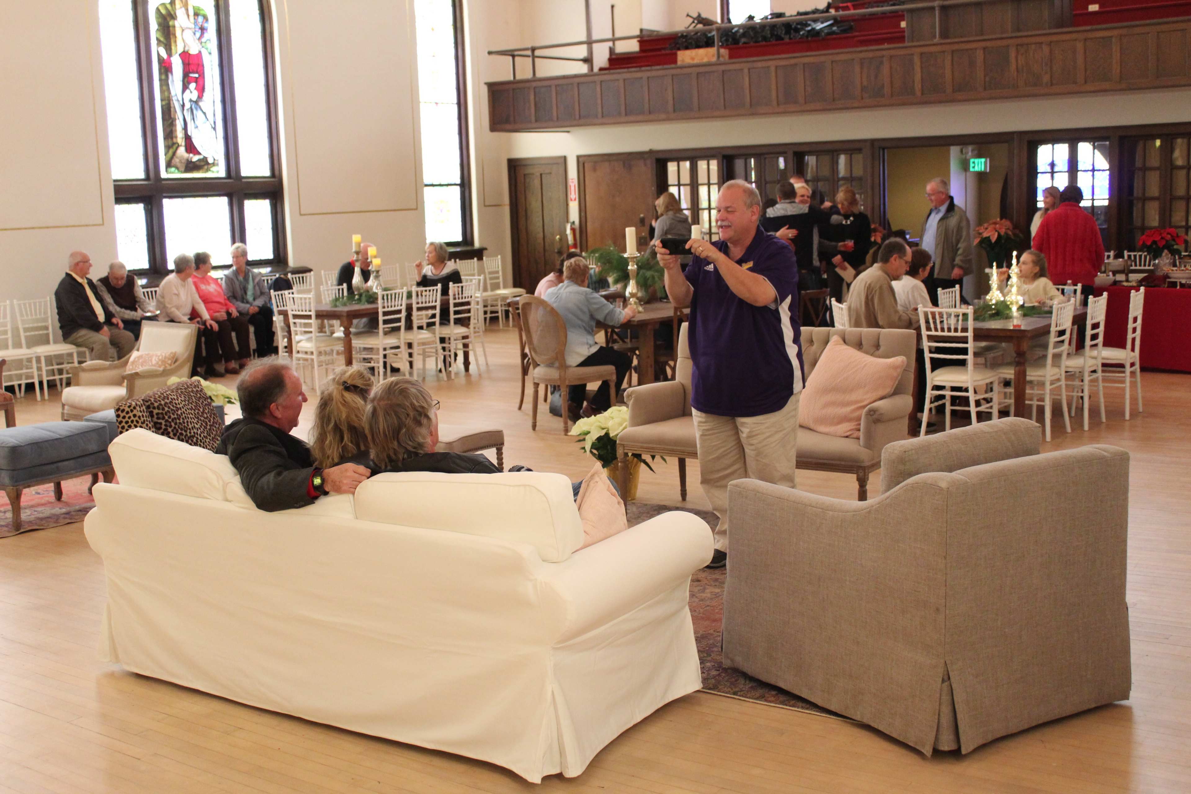 A group of attendees sits on sofas in a spacious event hall while others mingle in the background.