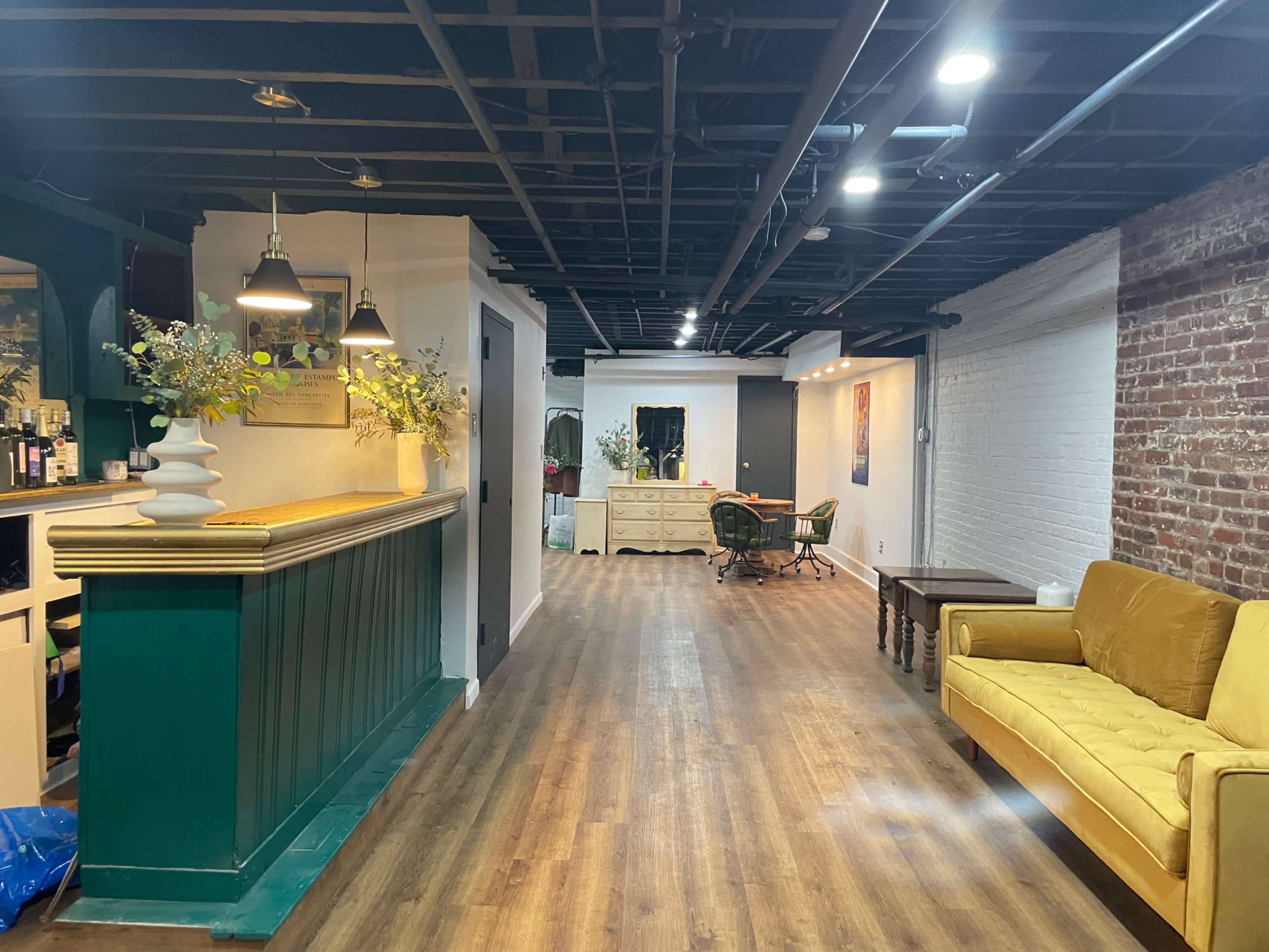 A spacious interior with a green reception desk on the left, a yellow couch, and a brightly lit area featuring vintage furniture in the background.