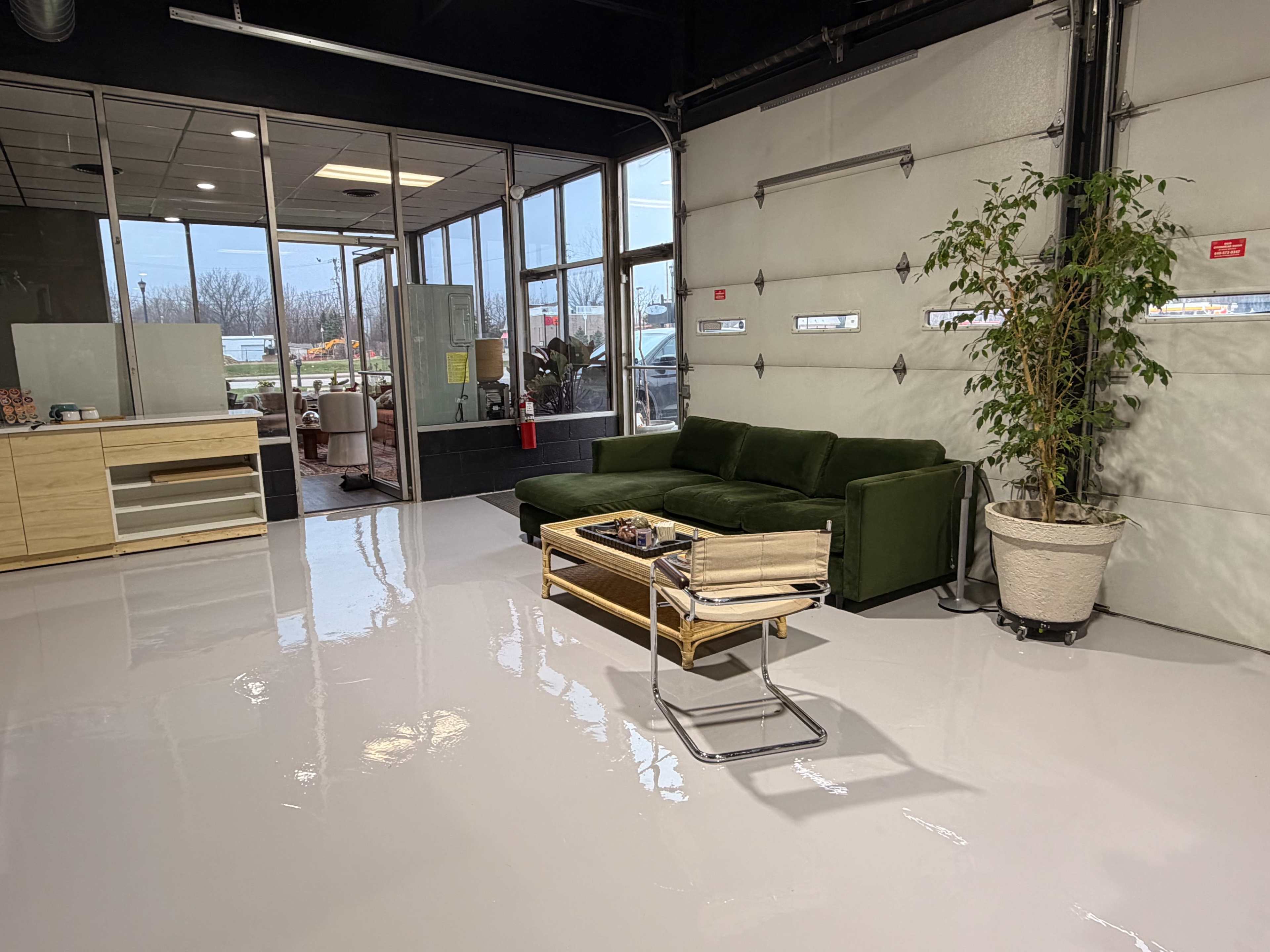 The image shows a modern interior space featuring a green couch, a wooden coffee table, a large potted plant, and a polished white floor.
