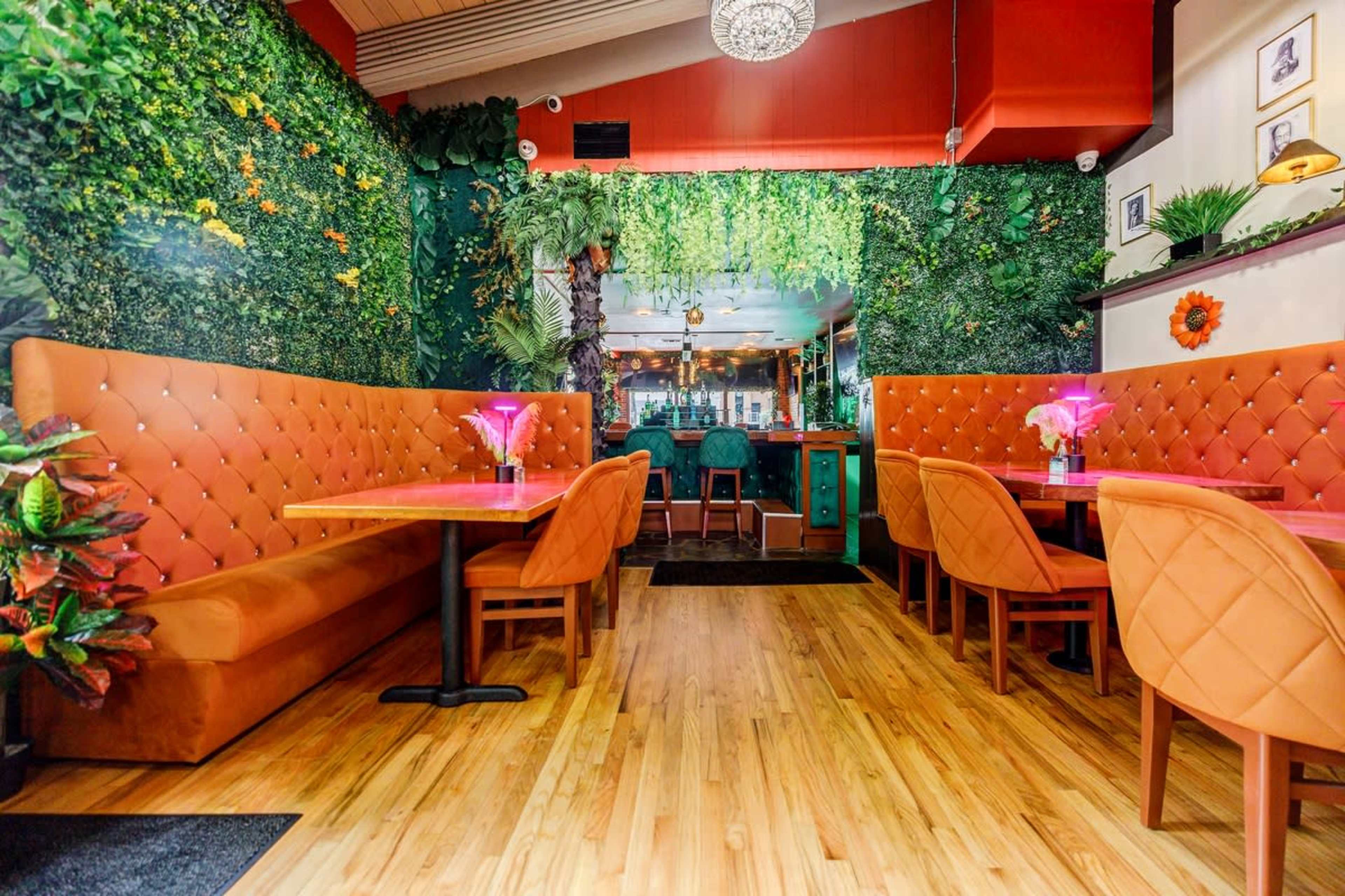 A vibrant restaurant interior featuring orange booths, wooden flooring, and a wall covered in greenery.