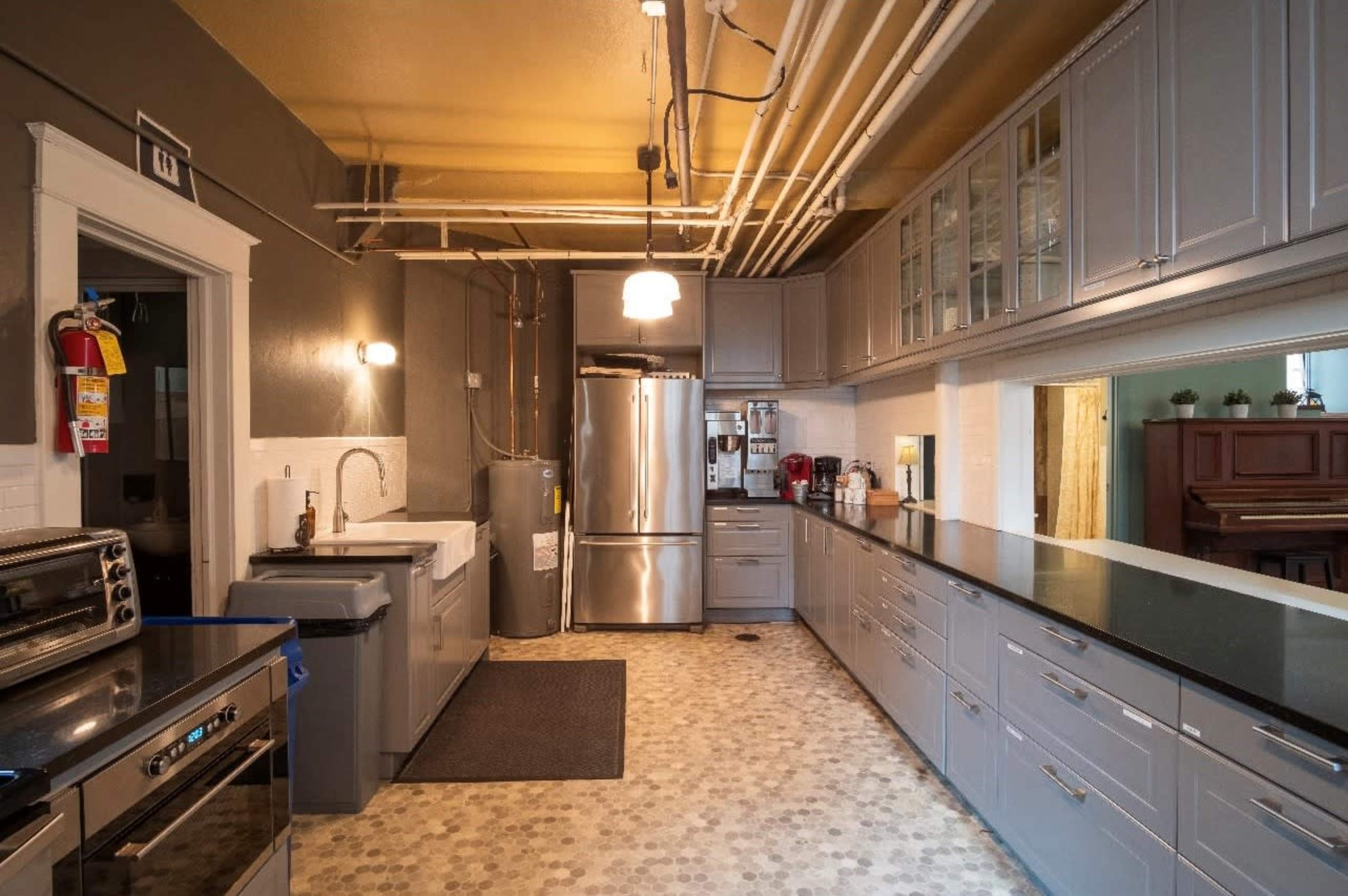 A modern kitchen features gray cabinetry, stainless steel appliances, a large sink, and a black countertop, with visible plumbing pipes overhead.